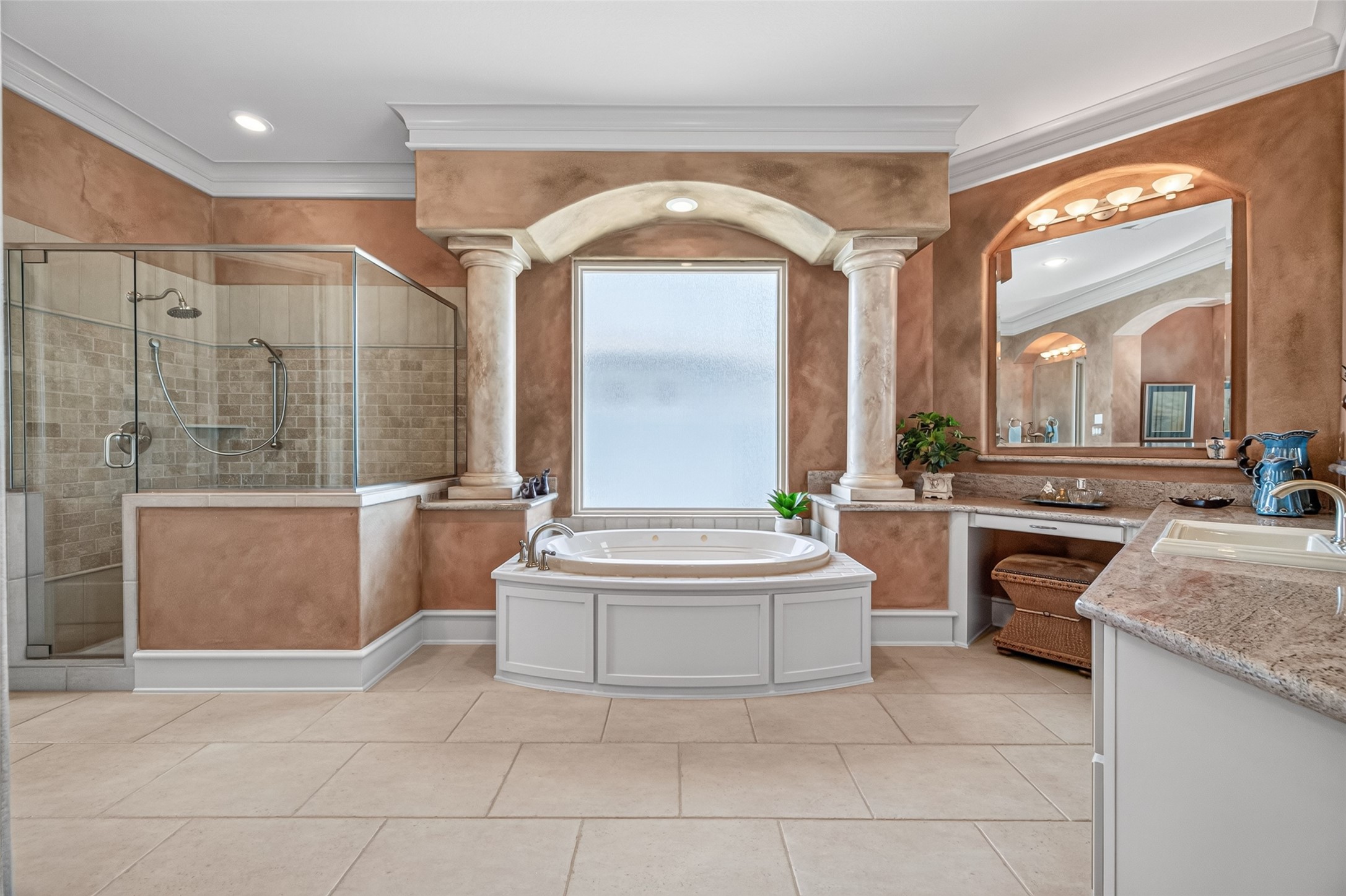 Luxurious bathroom featuring a central soaking tub framed by elegant columns, a spacious glass-enclosed shower, and dual vanities with rich granite countertops for a spa-like experience.