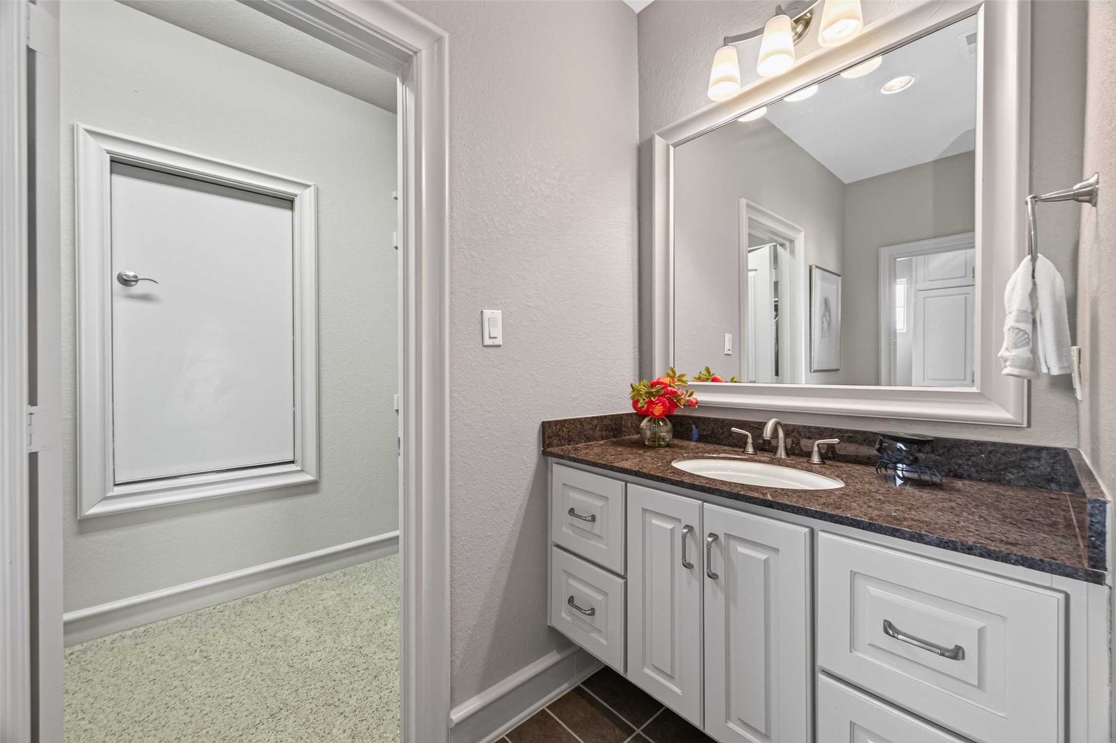 Elegant bathroom with a sleek vanity featuring dark granite countertops, ample storage, and a large framed mirror, complemented by soft overhead lighting for a tranquil ambiance.