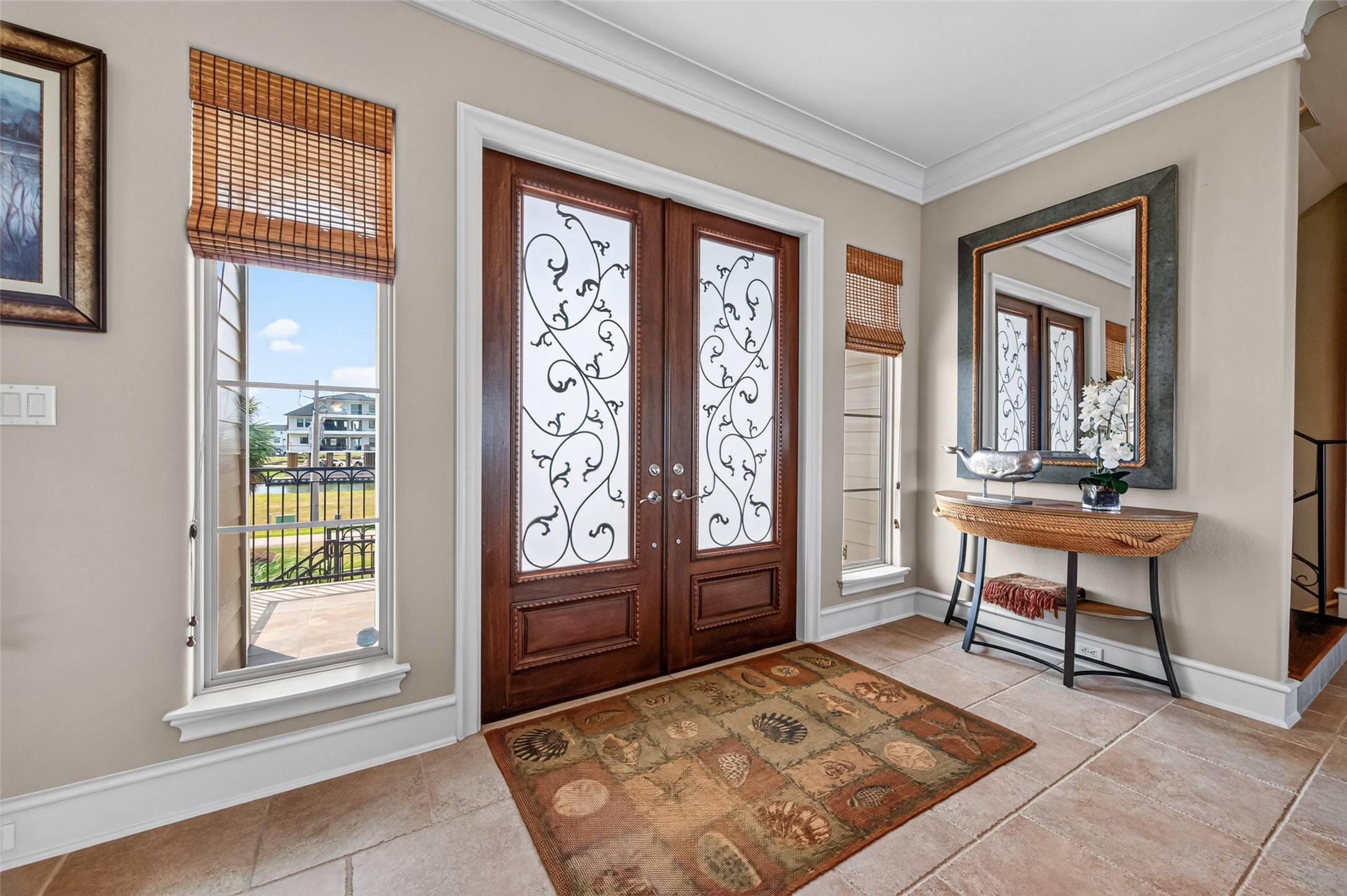 Elegant entryway featuring ornate double doors with decorative glass panels. Natural light streams through adjacent windows, highlighting a stylish console table and a large mirror, creating a welcoming and sophisticated atmosphere.