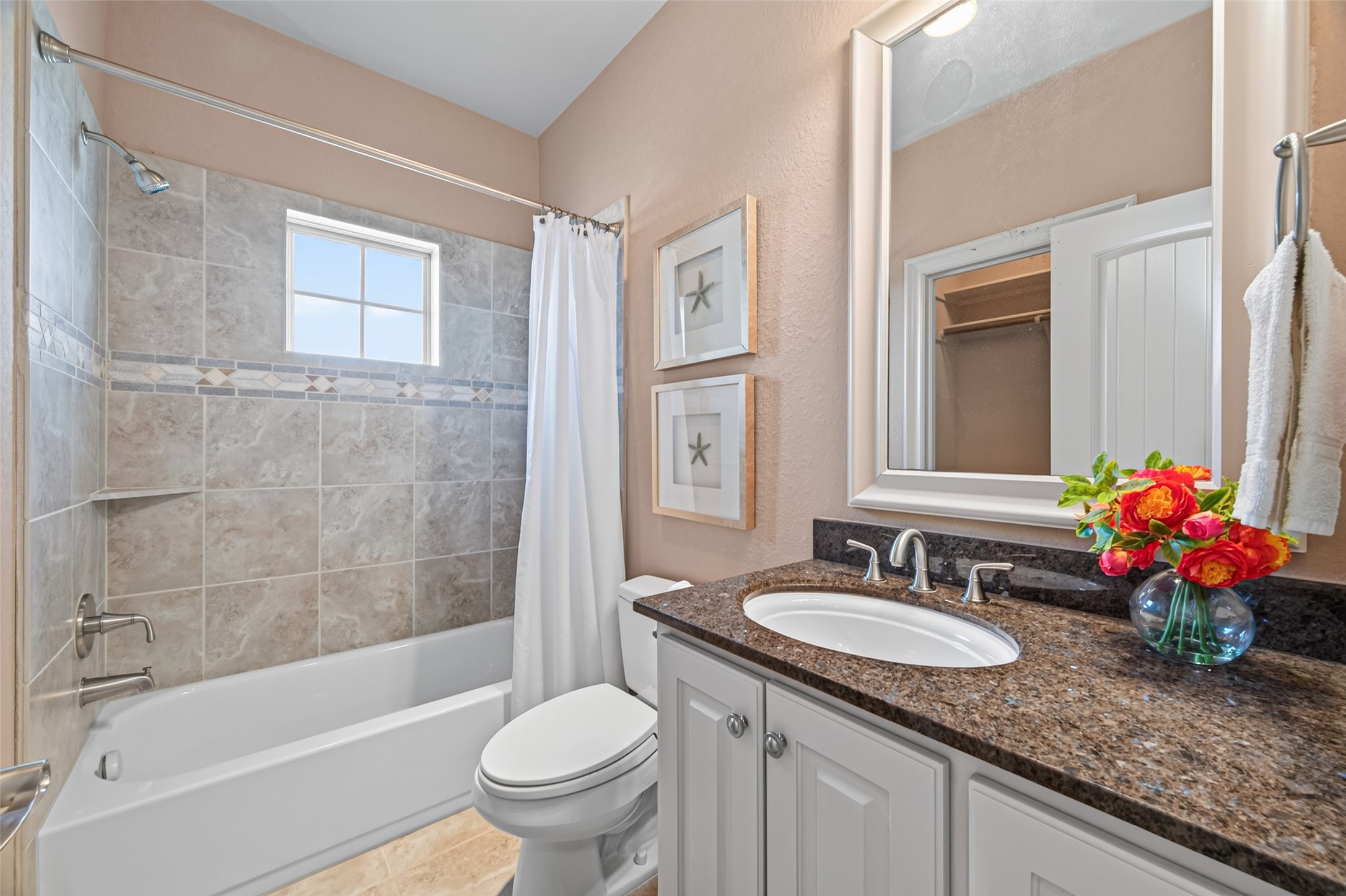 Charming bathroom with a granite-topped vanity, bright tile accents, and a shower-tub combo, enhanced by natural light from a window.
