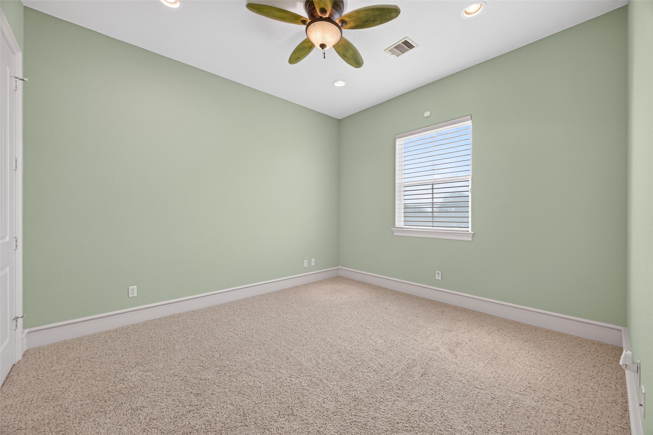 Cozy bedroom with soft green walls, plush carpet, and a ceiling fan, offering a serene and inviting atmosphere.