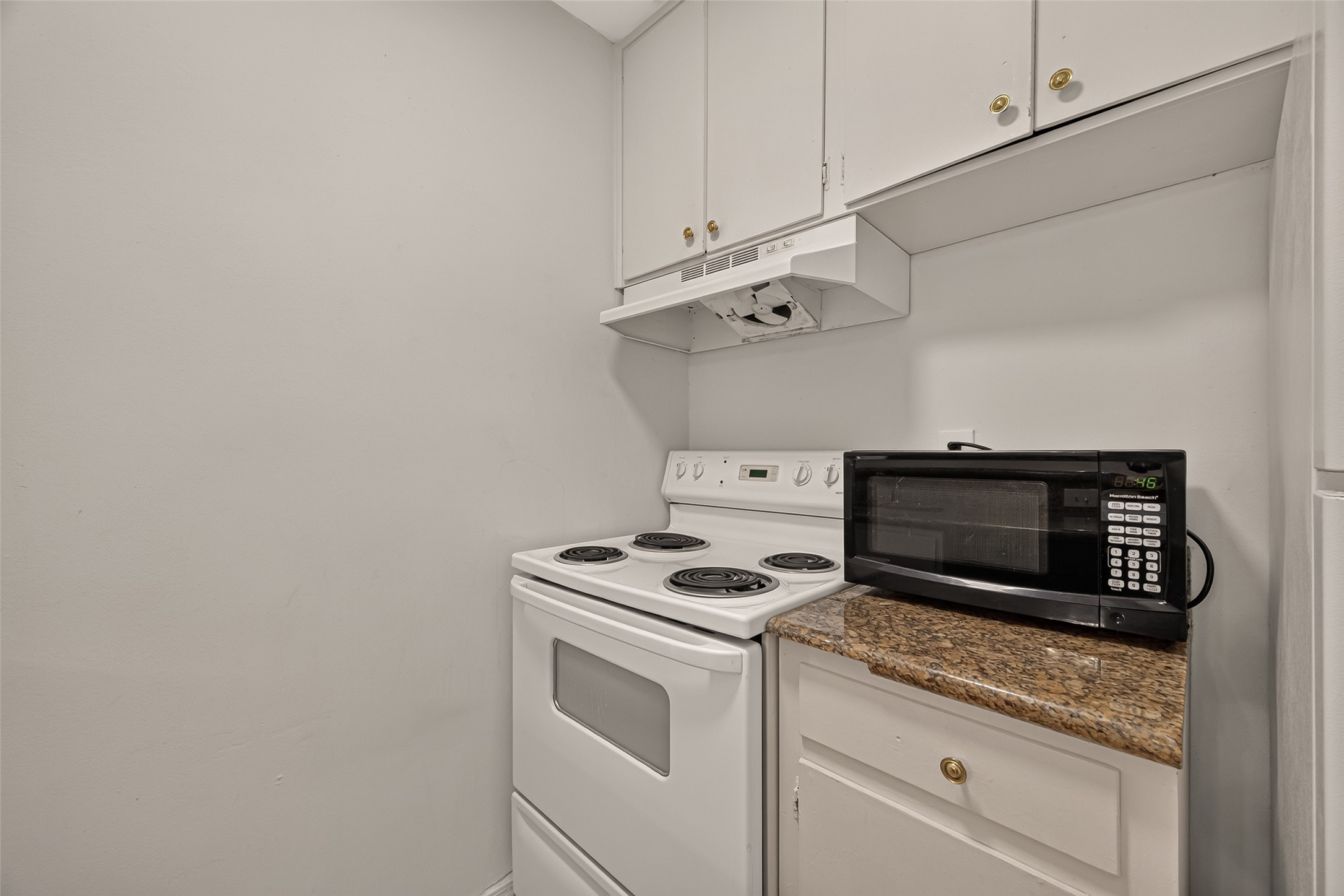Compact kitchen nook with an electric stove, granite countertop, and convenient overhead cabinets for storage.