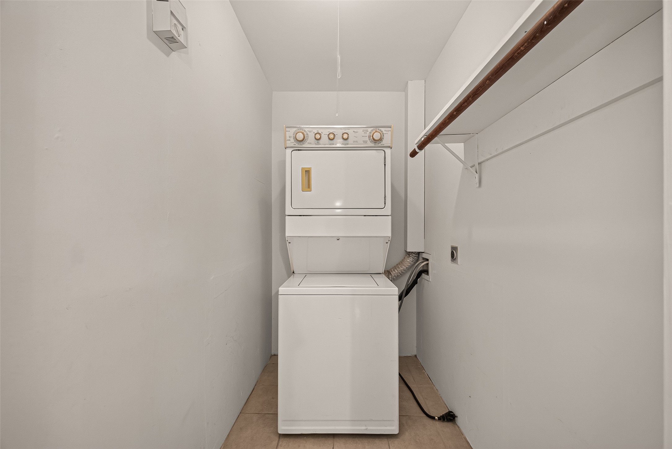 Compact laundry area featuring a stacked washer and dryer, with an adjacent hanging rod for convenient clothing organization.