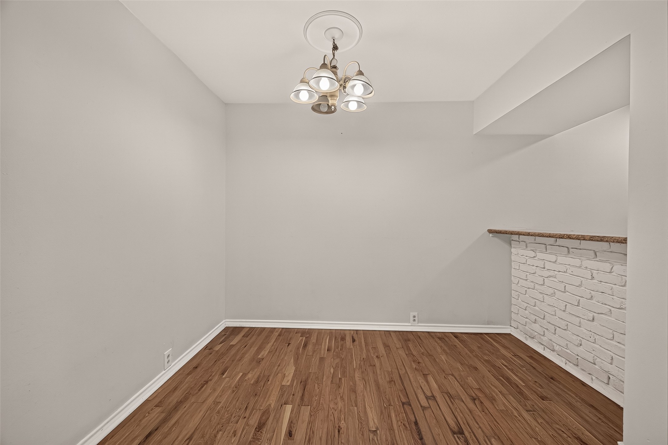 Charming dining area with warm hardwood floors and a stylish chandelier, featuring a cozy breakfast bar with a brick accent wall.