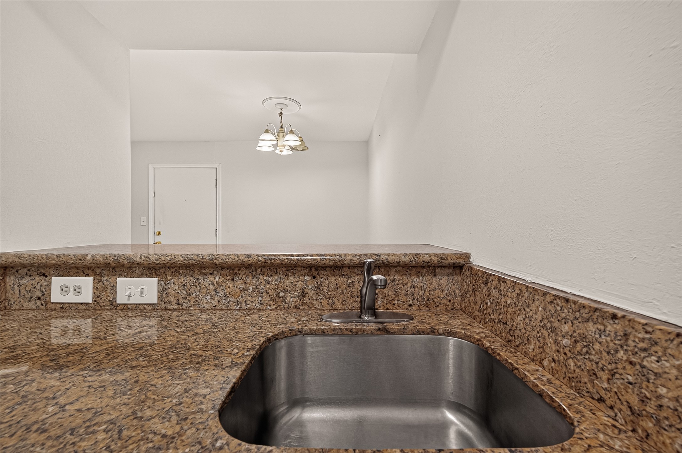 Elegant granite countertops with a built-in stainless steel sink provide a sleek and functional kitchen space, complemented by modern lighting fixtures.