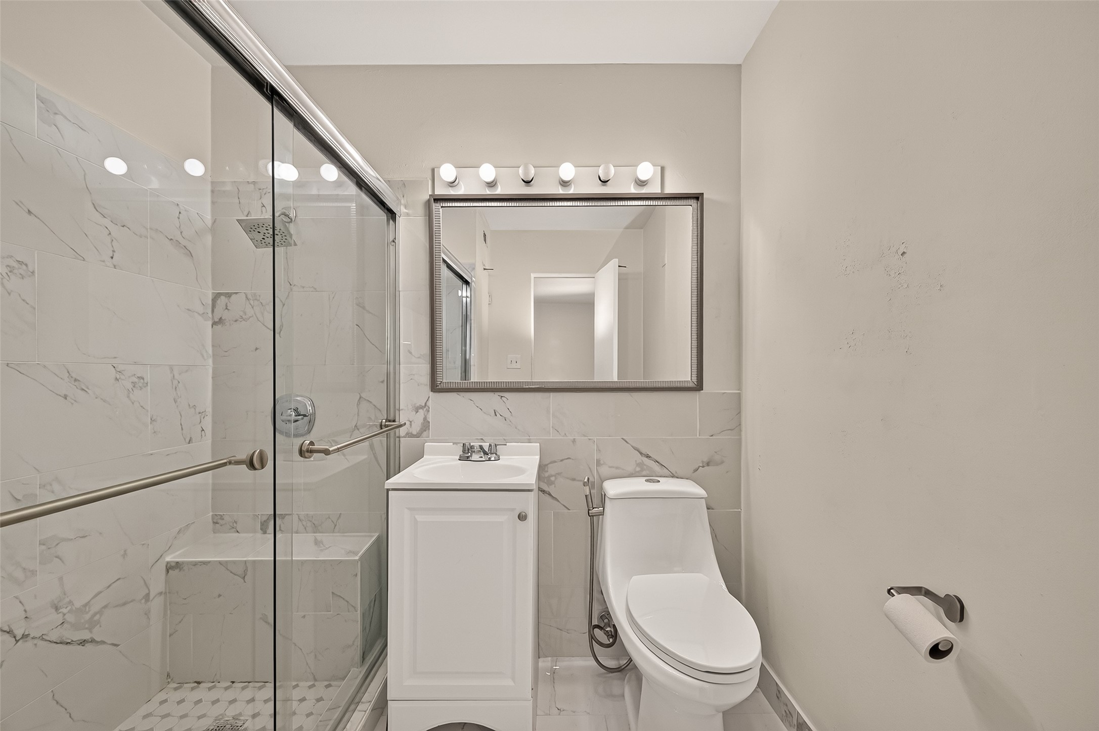 Sleek bathroom featuring a glass-enclosed shower with elegant marble tiles, a modern vanity, and ample lighting for a bright and inviting space.