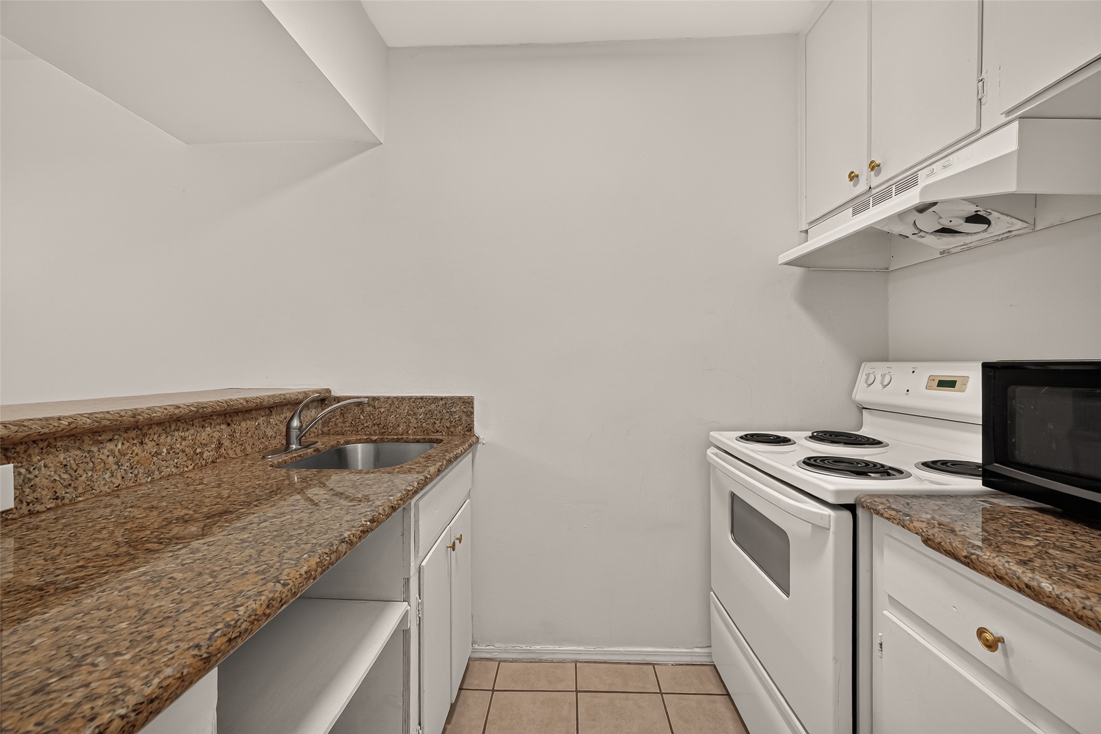 Compact kitchen featuring sleek granite countertops, a white electric stove, and ample cabinetry for storage.