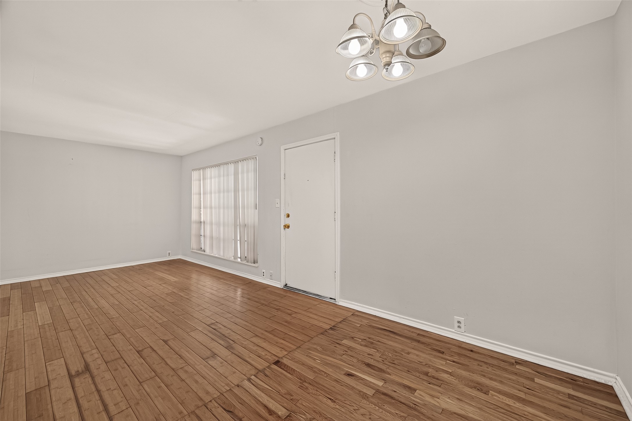 Bright and spacious room featuring elegant hardwood floors, neutral walls, and a stylish light fixture, creating a welcoming atmosphere.