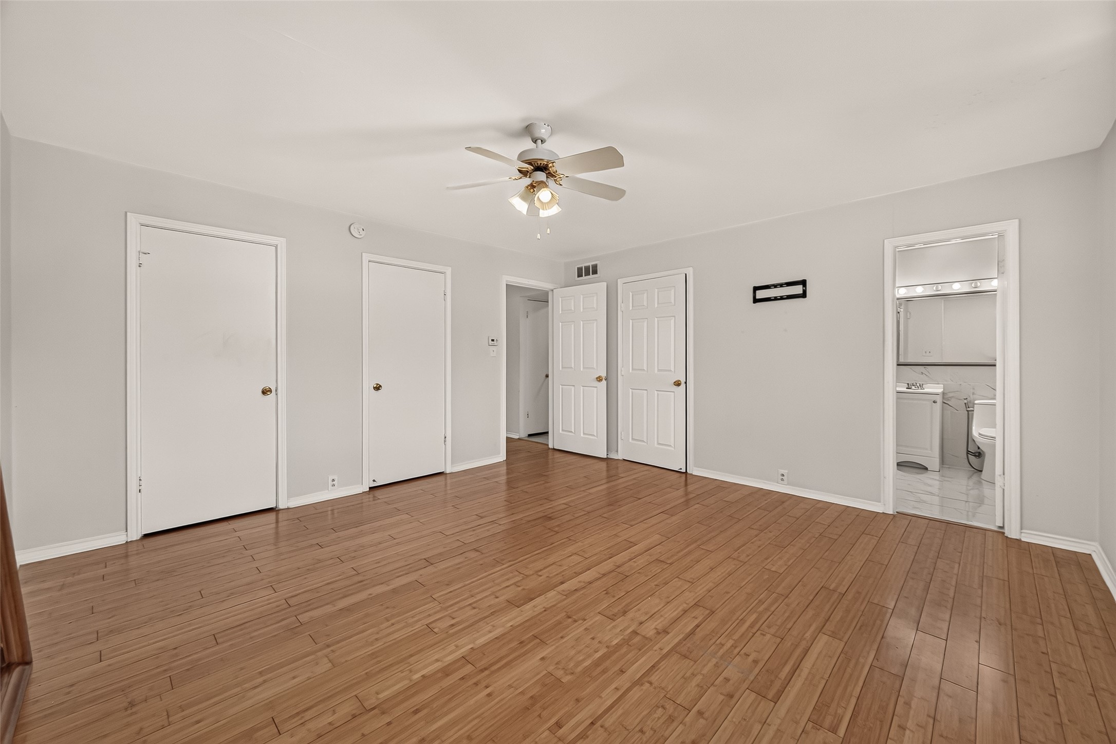 Spacious room with polished hardwood floors, a ceiling fan, and ample closet space, leading to an en-suite bathroom.