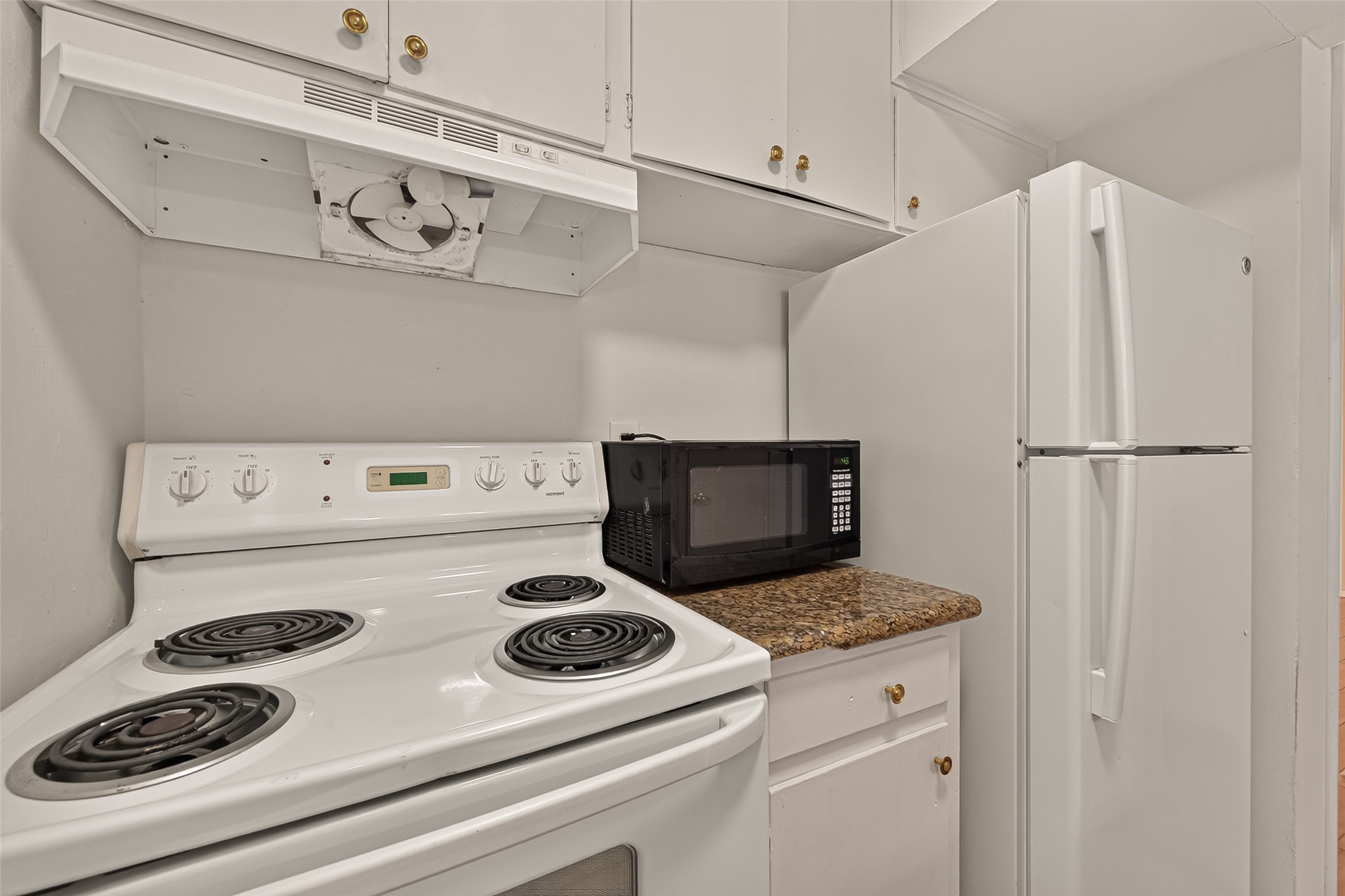 Compact kitchen with a cozy layout, featuring a white electric stove, a sleek microwave on granite countertops, and ample cabinet storage, ideal for efficient cooking.