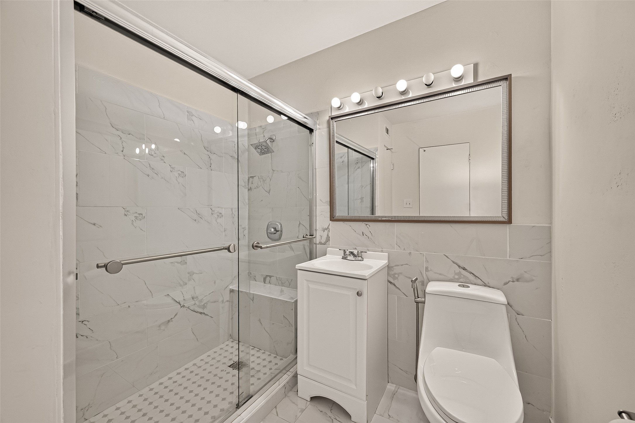 Elegant bathroom featuring a sleek glass-enclosed shower with modern marble tile, a chic vanity with ample lighting, and a contemporary toilet for a sophisticated touch.