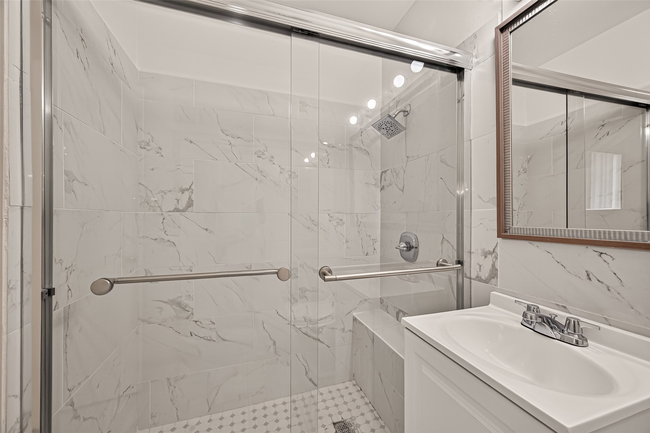 Elegant bathroom featuring a spacious glass-enclosed shower with marble-style tiles and a sleek vanity, offering a modern and luxurious feel.