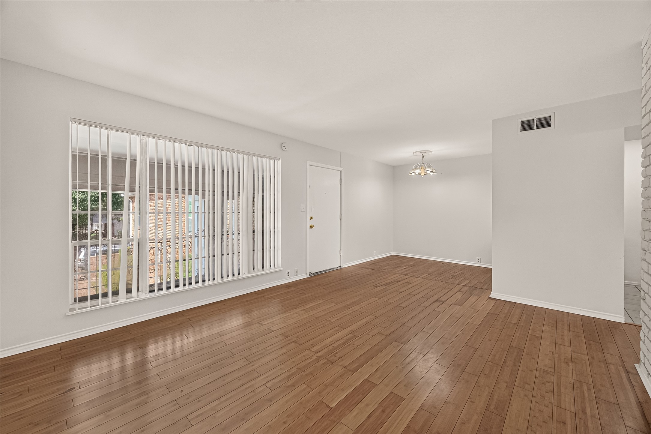 Spacious living area with warm wooden flooring and ample natural light from a large window, creating an inviting atmosphere.