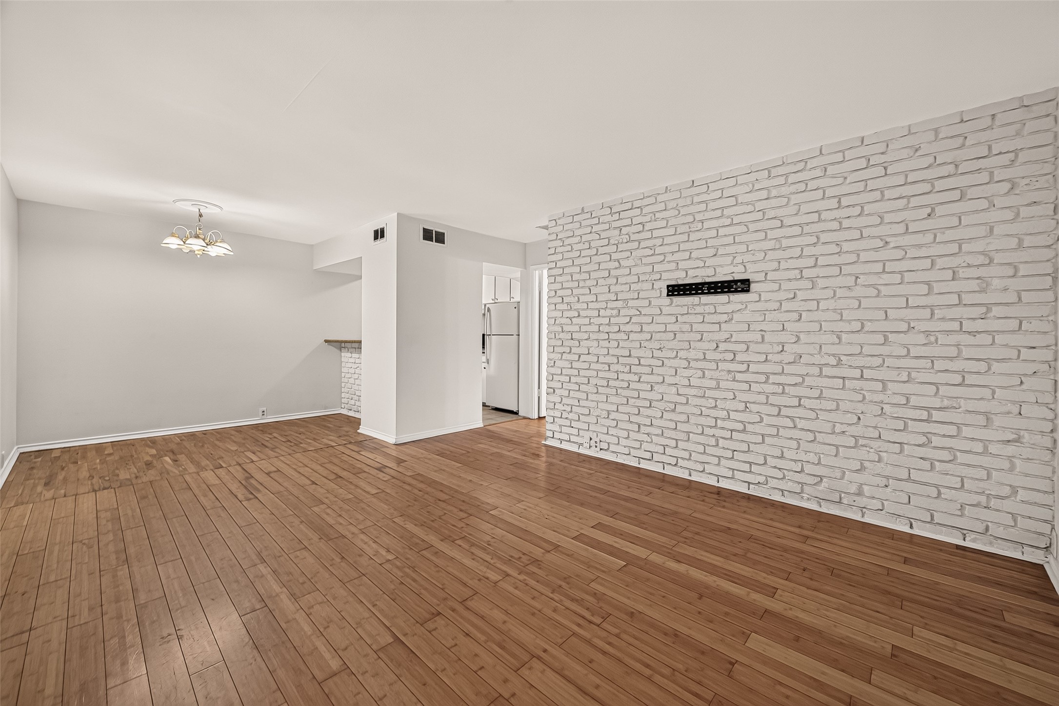 Spacious living area with elegant hardwood floors and a striking white brick accent wall, offering a modern and inviting atmosphere.