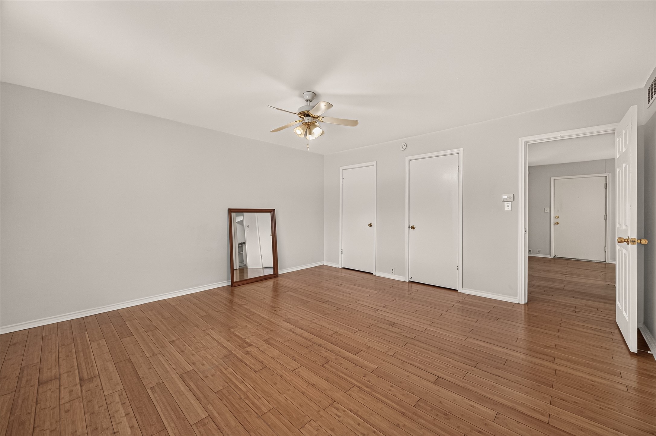 Spacious room with elegant hardwood flooring, neutral walls, and a ceiling fan, offering ample natural light and versatile layout options.