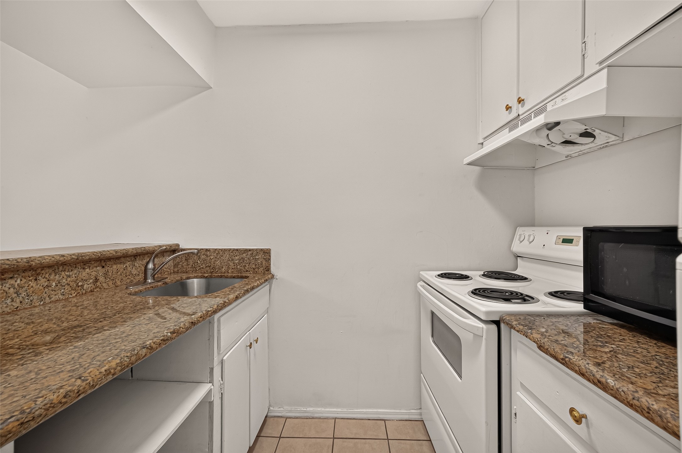 Compact kitchen with elegant granite countertops, white cabinetry, and a modern electric stove, offering efficiency and style.