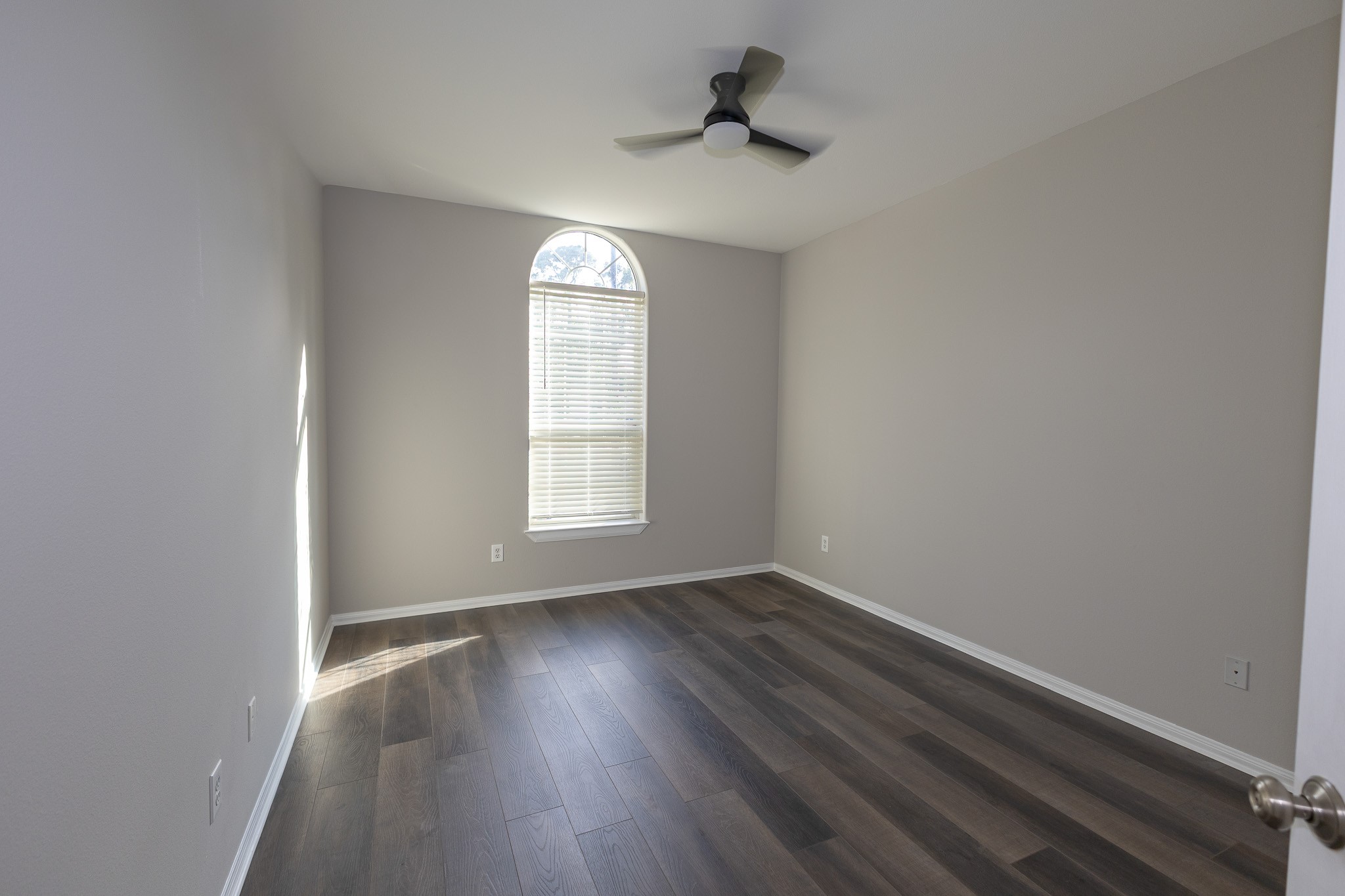 Bright and inviting bedroom featuring beautiful new flooring, fresh neutral paint, and a charming arched window that fills the space with natural light. A modern ceiling fan adds comfort and style!