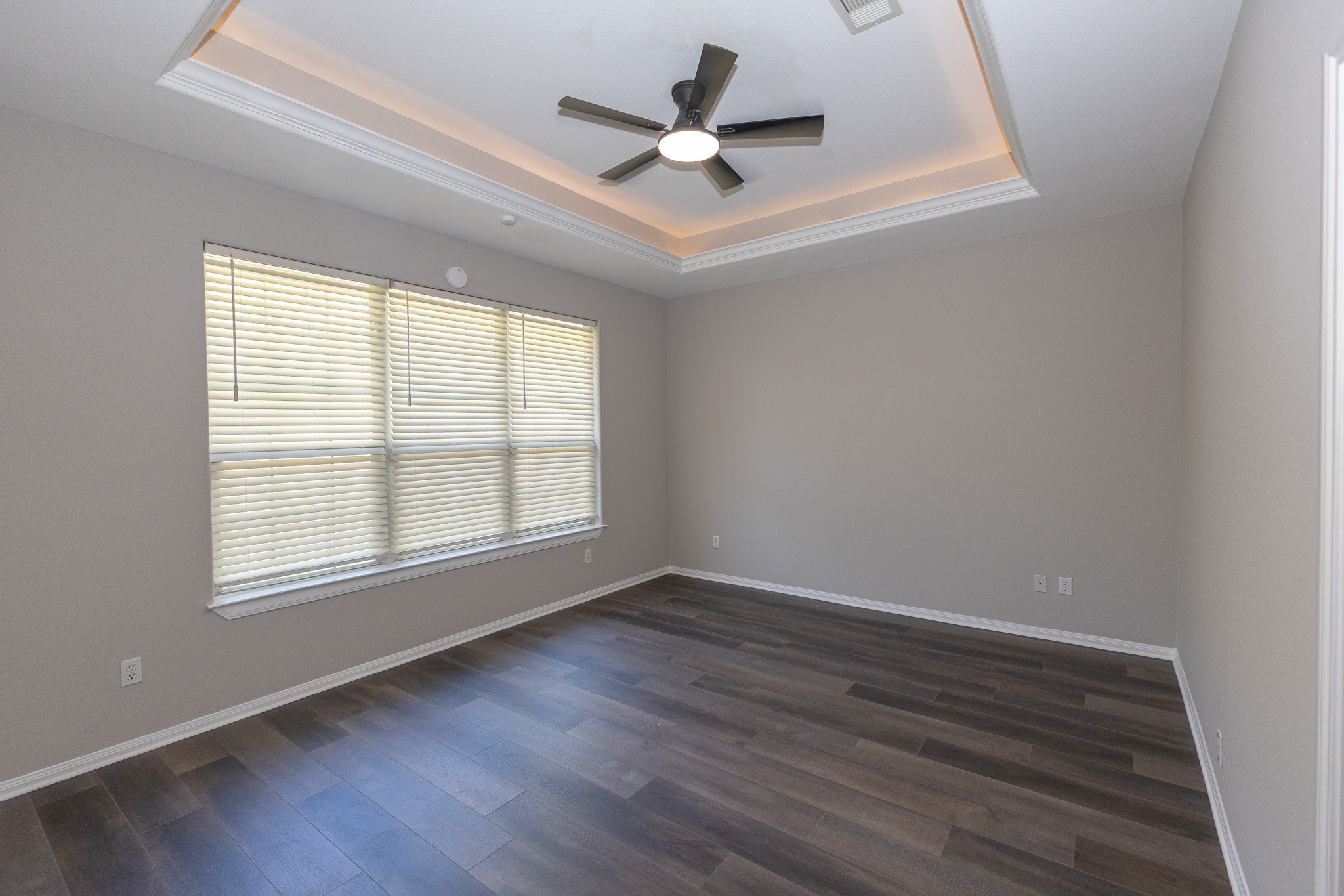 Spacious primary bedroom featuring beautiful new flooring, fresh neutral paint, and an elegant tray ceiling with soft accent lighting. Large windows fill the room with natural light, creating a peaceful retreat to unwind at the end of the day!