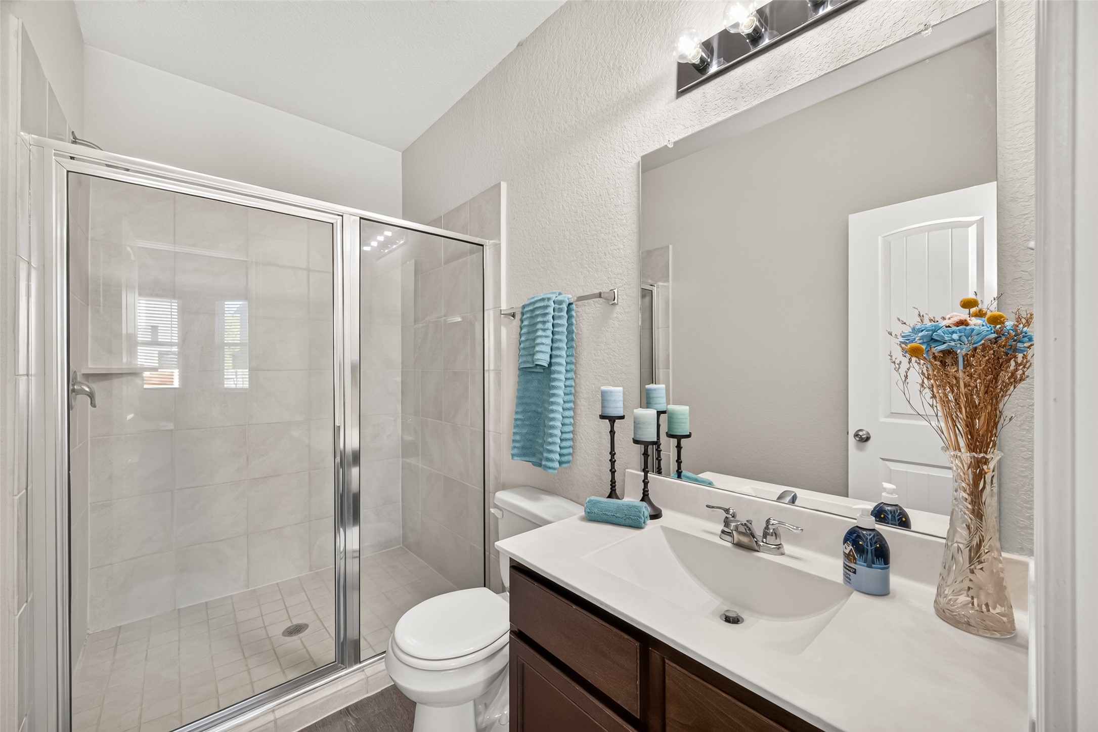 Primary bath offering bright and modern bathroom featuring a spacious glass-enclosed shower, elegant vanity with stylish lighting, and tasteful decor accents.