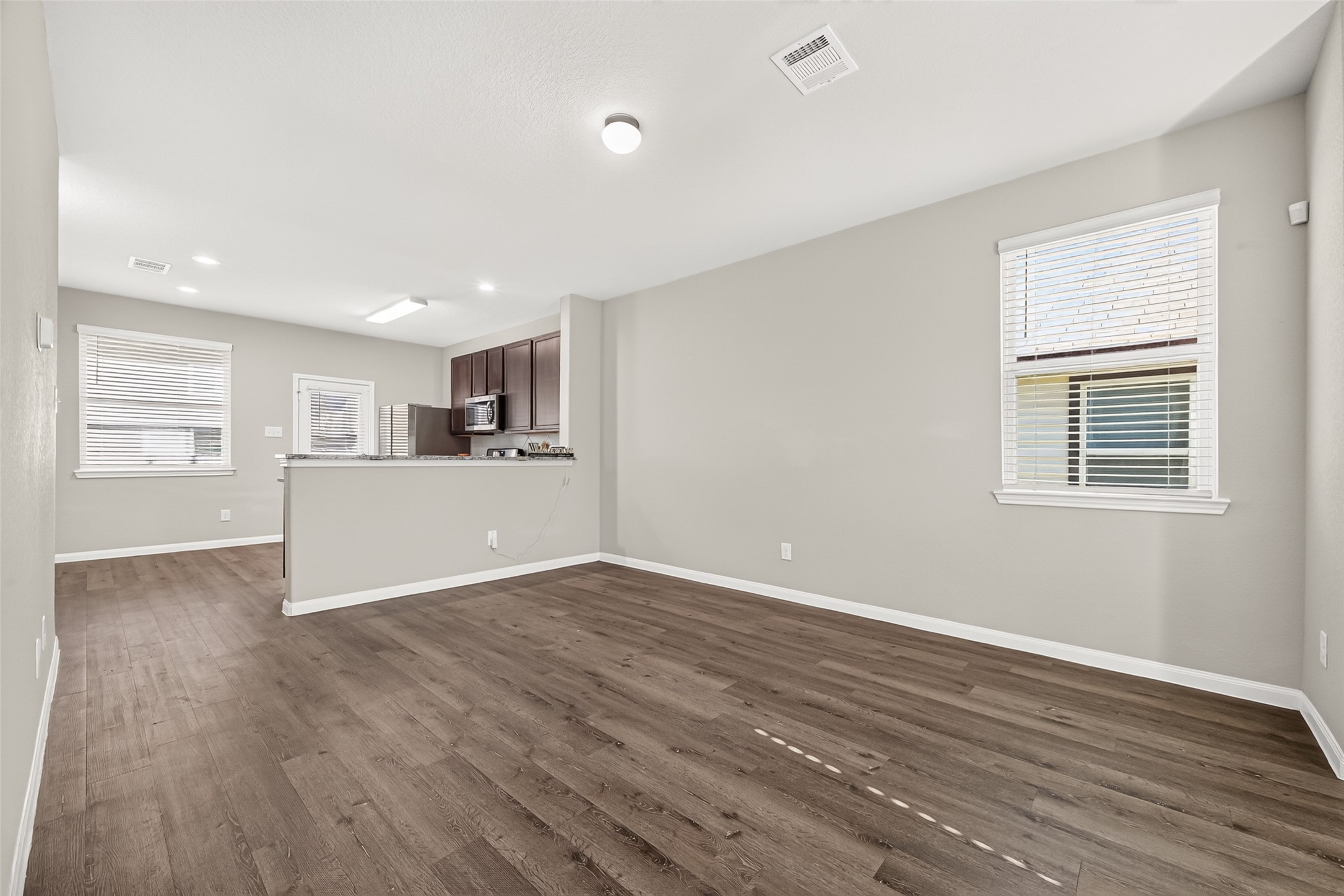 Spacious open-concept living area with elegant flooring and abundant natural light, seamlessly flowing into a modern kitchen with dark cabinetry.