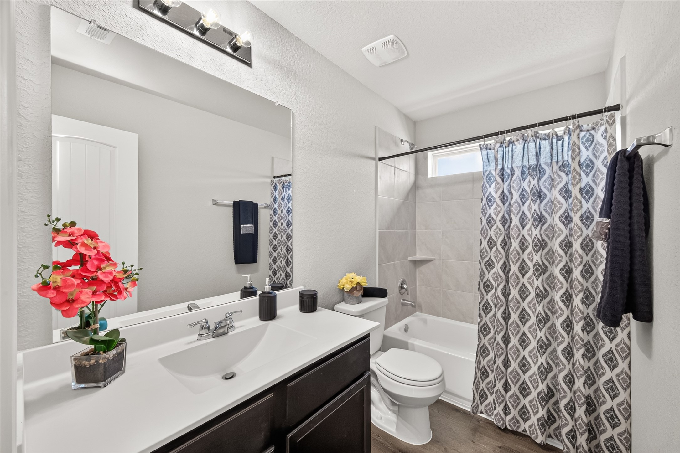 Modern bathroom with a stylish vanity, chic lighting, and a bathtub with an elegant patterned shower curtain.