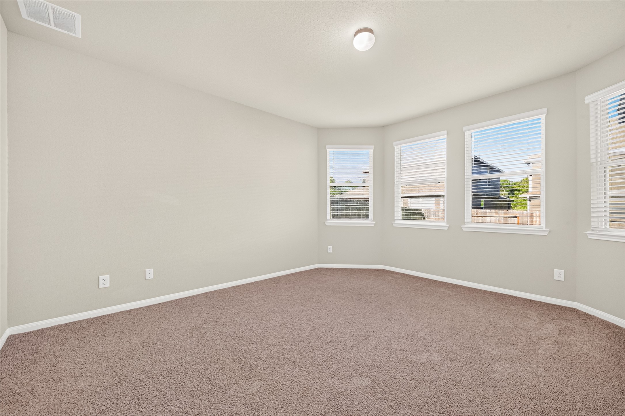 Primary bedroom with extended window space for a reading nook. Light-filled room with neutral walls, plush carpet, and multiple large windows offering a serene view.