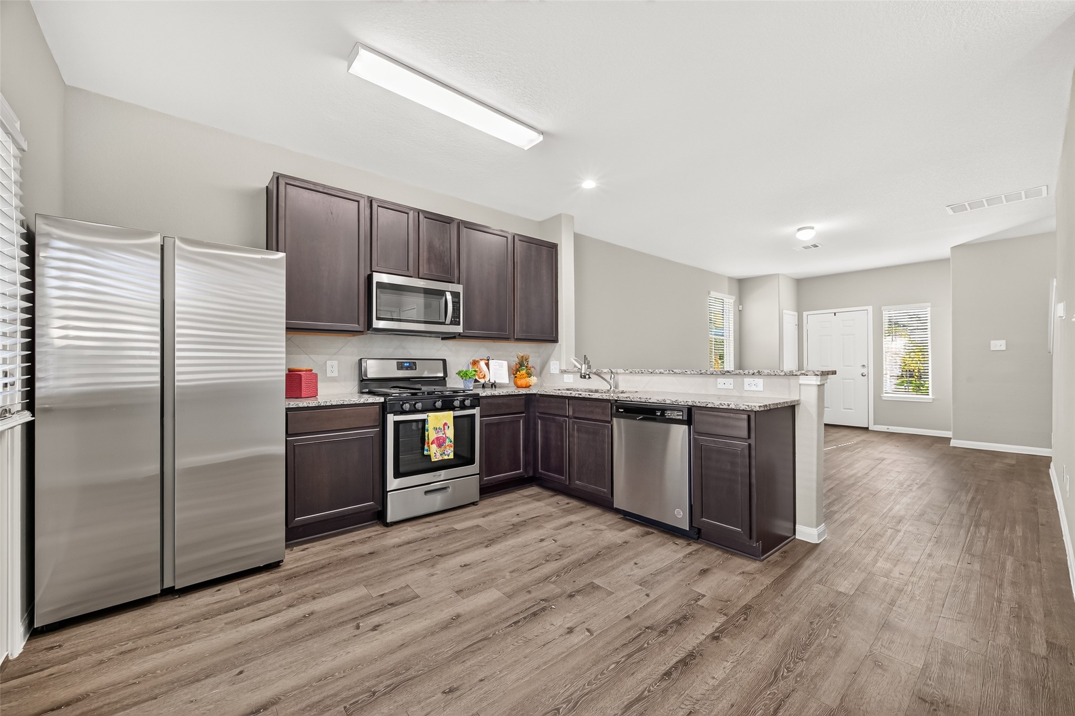 Modern kitchen with stainless steel appliances, dark cabinetry, and a spacious open layout leading into a bright living area.