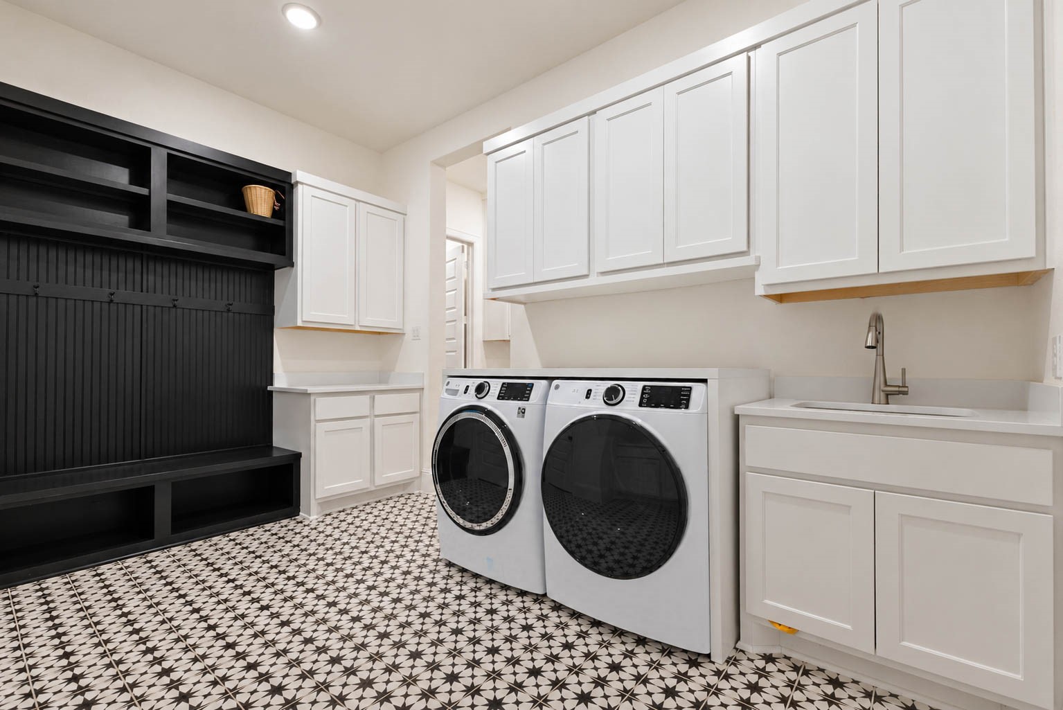 Stylish laundry room featuring modern appliances, ample cabinetry, a convenient sink, and a chic black and white tile floor. Cute accent with black mud room coming from the garage.