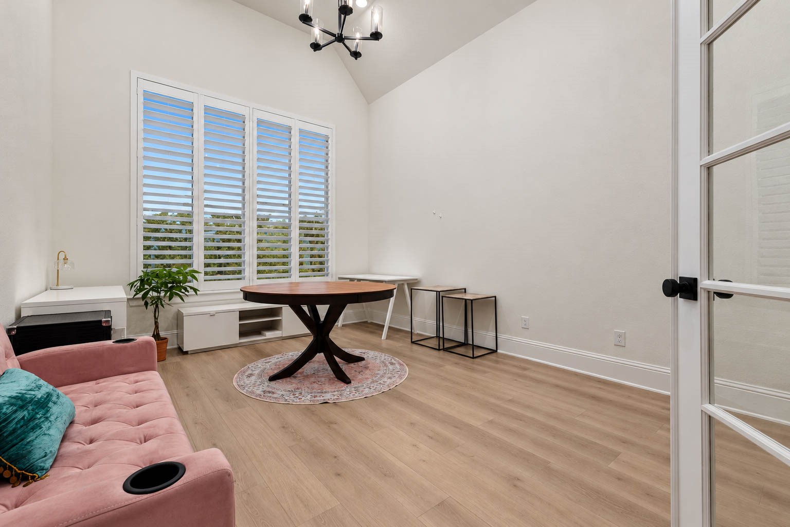 Charming home office space with high ceilings, featuring elegant wood flooring and abundant natural light streaming through large plantation shutters. Enclosed by glass french doors.