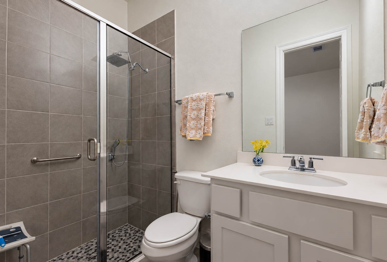 Modern bathroom featuring a spacious glass-enclosed shower with sleek gray tiles, a white vanity with ample storage, and a large mirror, creating a bright and inviting space.