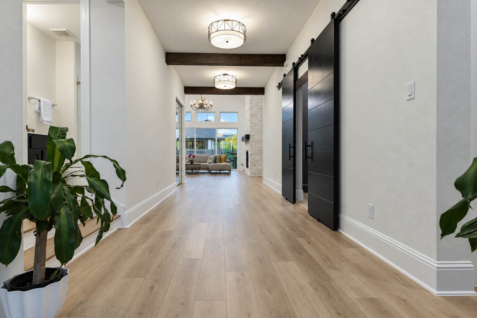 Elegant hallway featuring sleek wood flooring and modern light fixtures, leading to a spacious living area with large windows and a cozy fireplace. Elegant hallway featuring sleek wood flooring and modern light fixtures, leading to a spacious living area with large windows and a cozy fireplace.