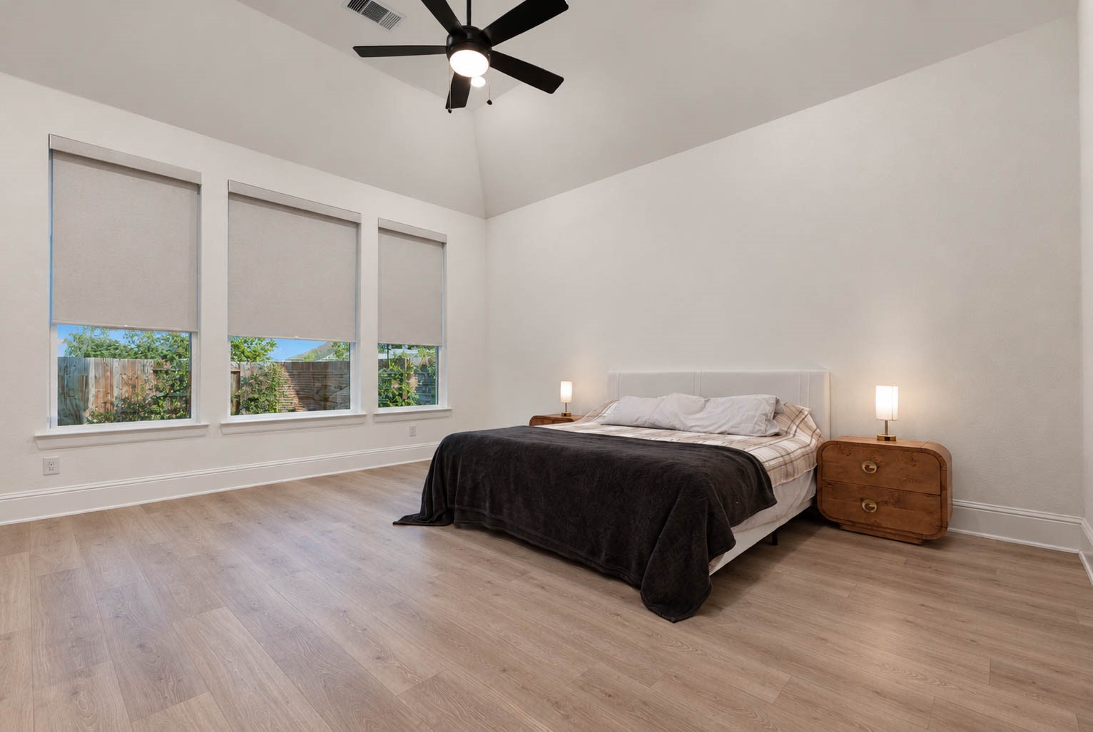 Spacious primary bedroom with high ceilings, large windows with custom blinds, and elegant wood flooring, featuring a modern ceiling fan and ample natural light.