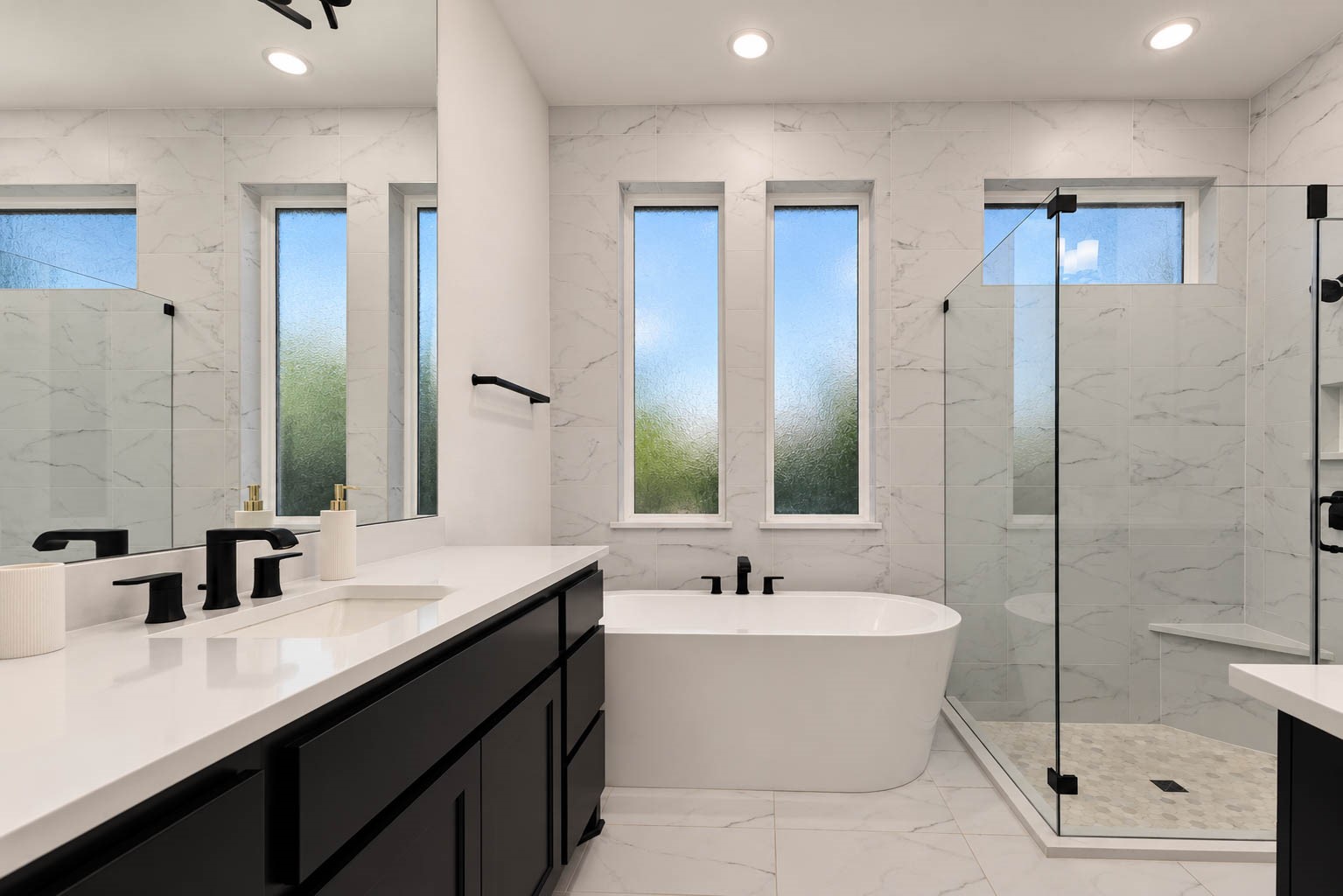 Elegant primary bathroom featuring a freestanding soaking tub, sleek glass shower, and modern black fixtures, complemented by marble-patterned tiles and abundant natural light through tall windows.