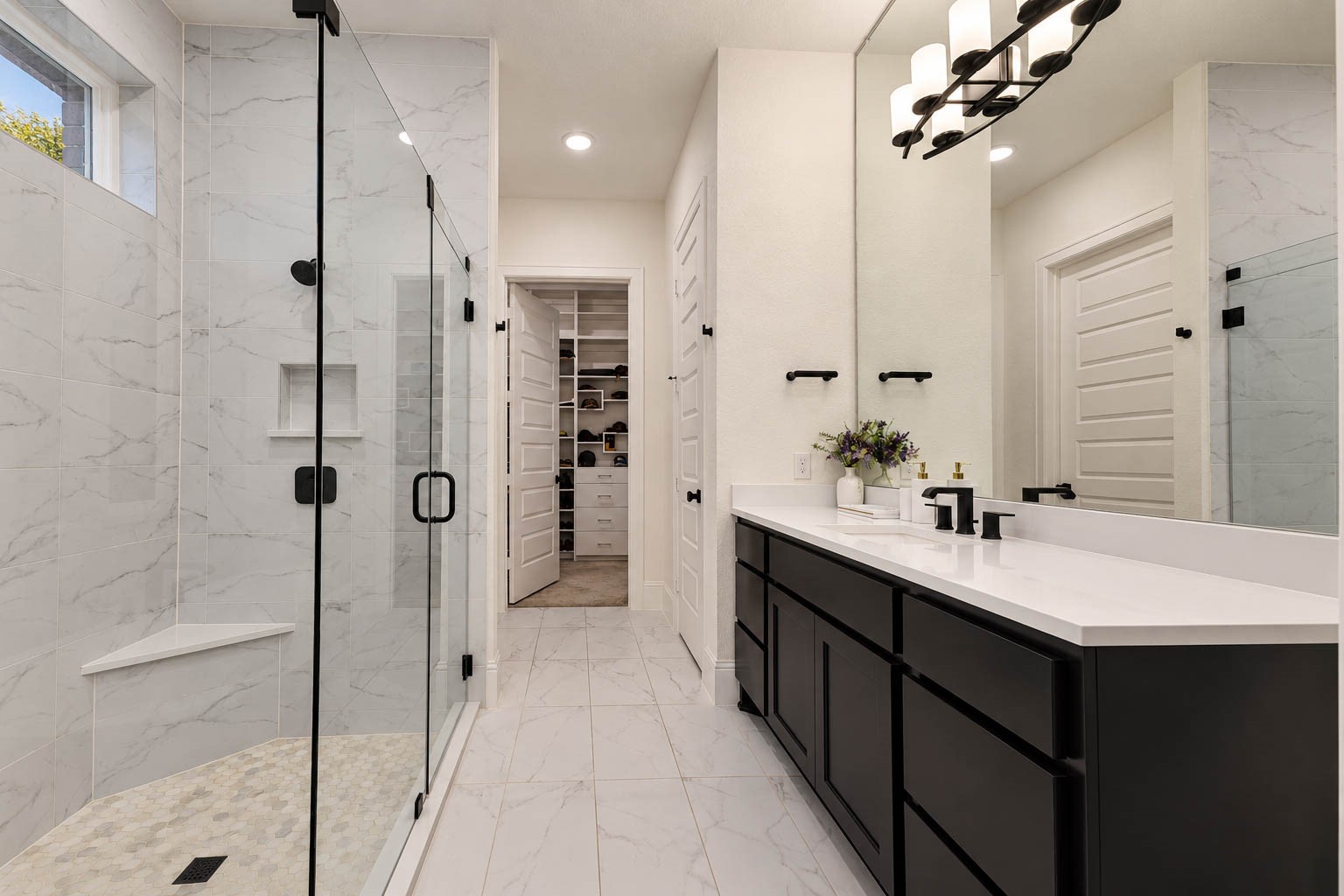 Elegant bathroom featuring a spacious glass-enclosed super shower with marble-like tile, a sleek double vanity with modern fixtures, and access to a convenient walk-in closet.