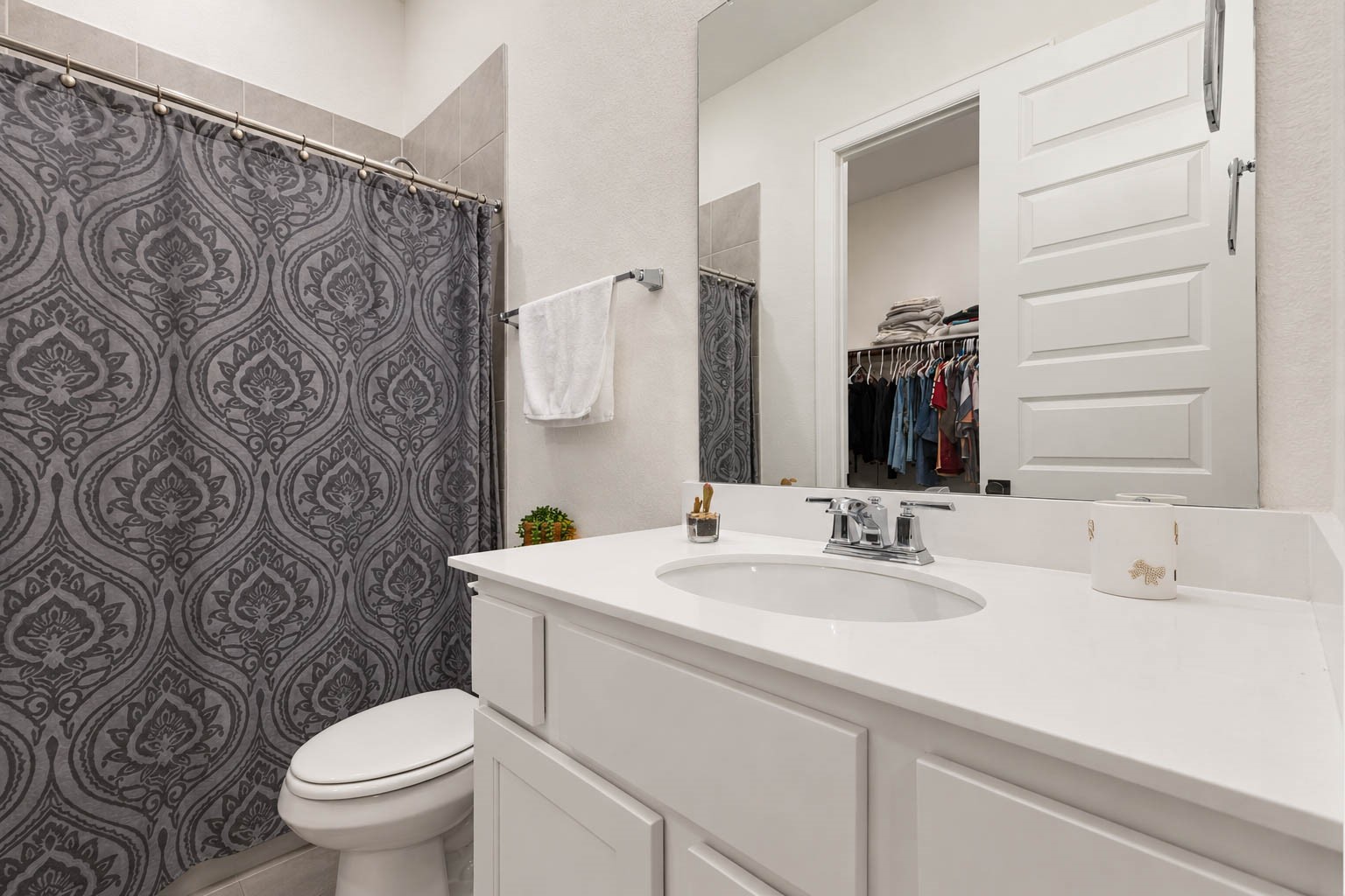 Chic bathroom with a sleek white vanity, elegant patterned shower curtain, and ample storage, offering a modern and functional space.