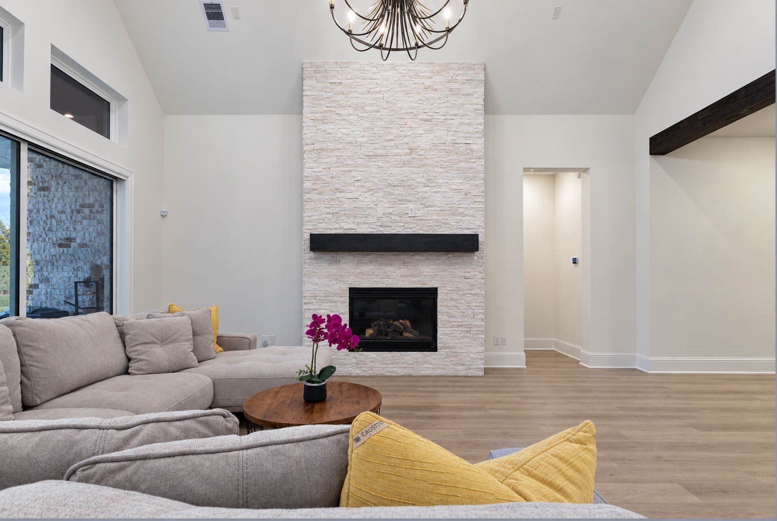 Bright and inviting living room featuring a stunning stone fireplace, high ceilings, and large windows that fill the space with natural light.