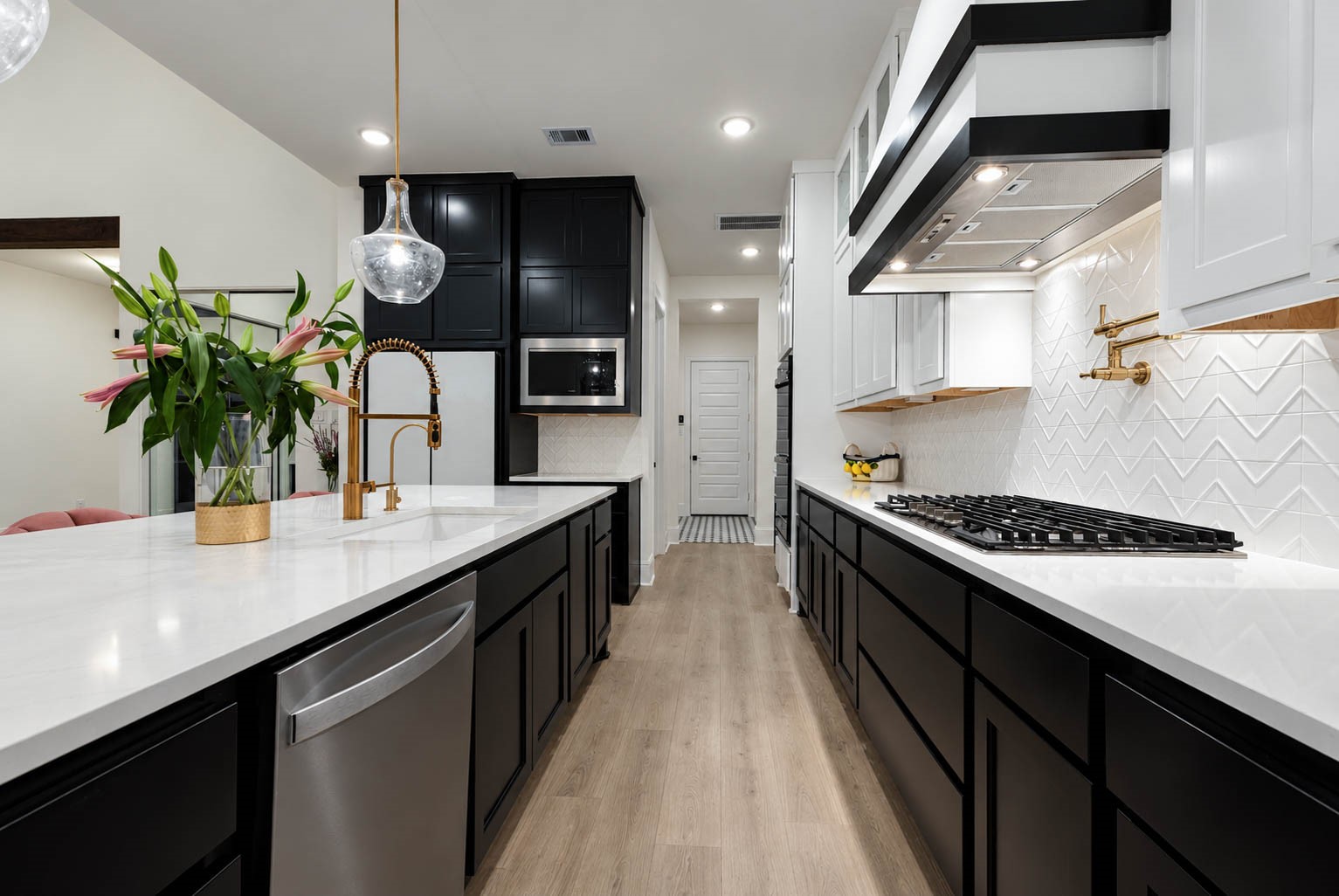Sleek modern kitchen featuring a spacious design with elegant black and white cabinetry, a stylish gold faucet, and a chic herringbone backsplash. Look at the pot filler in golden tones, just elegant and functional.