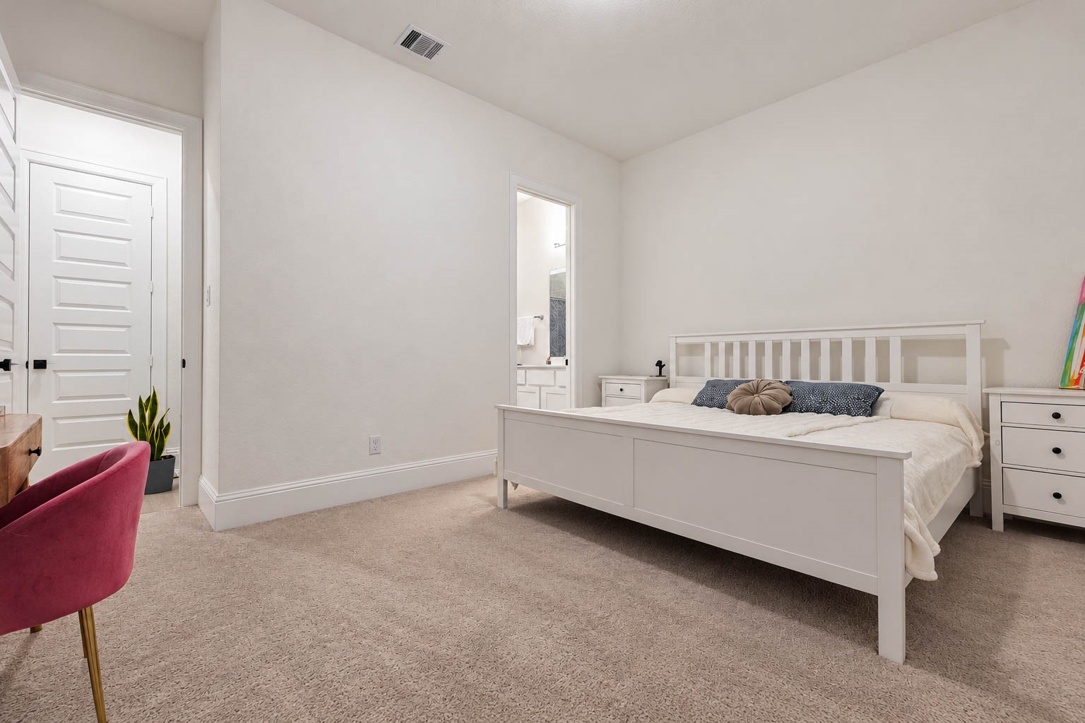 Spacious and inviting bedroom featuring plush carpeting, a stylish white bed frame, and a convenient en-suite bathroom, perfect for relaxation and comfort.