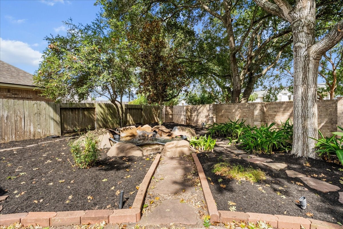 Landscaped backyard with stone-edged beds, a pond feature, and big mature trees.