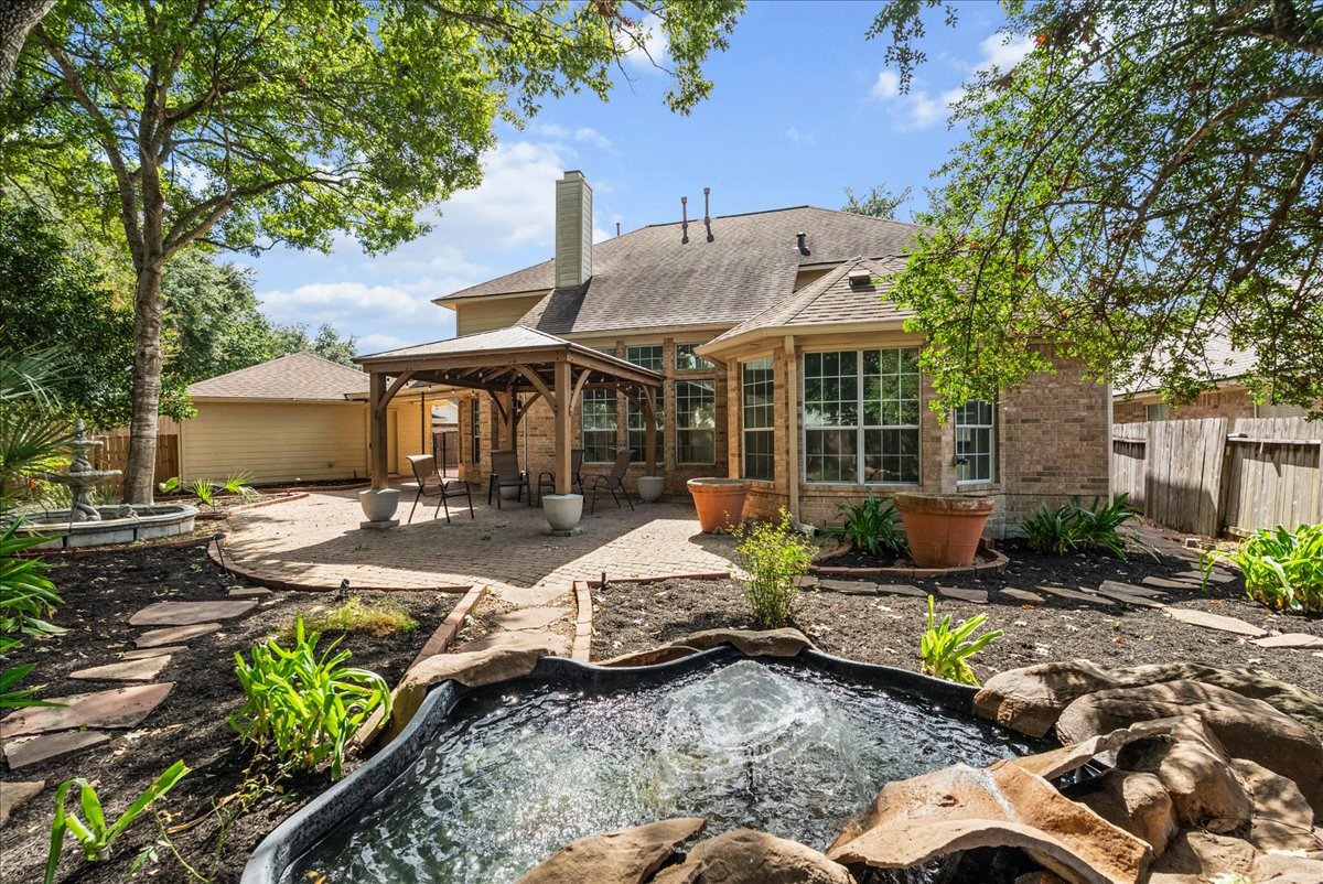 Private backyard retreat with a serene water feature, oversized pergola, and paver patio under large shade trees.