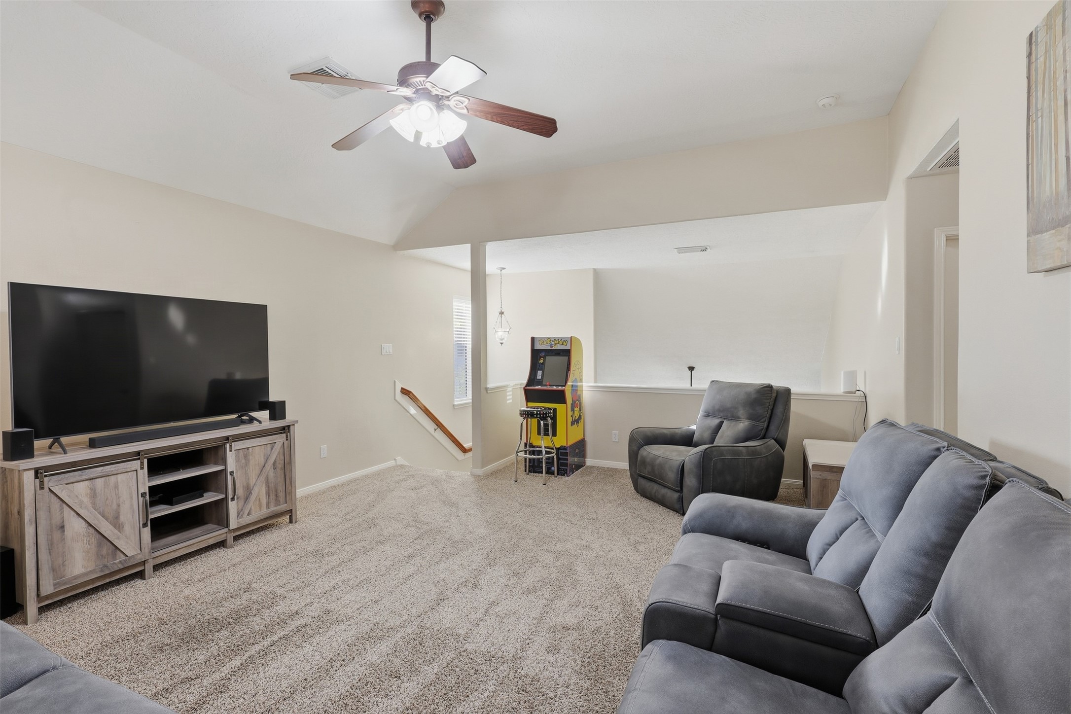 Another view of the generous upstairs game room showcases its versatile layout, comfortable seating area, plush carpeting, ceiling fan, and large windows. A wonderful space for entertaining guests or creating a dedicated family recreation area.