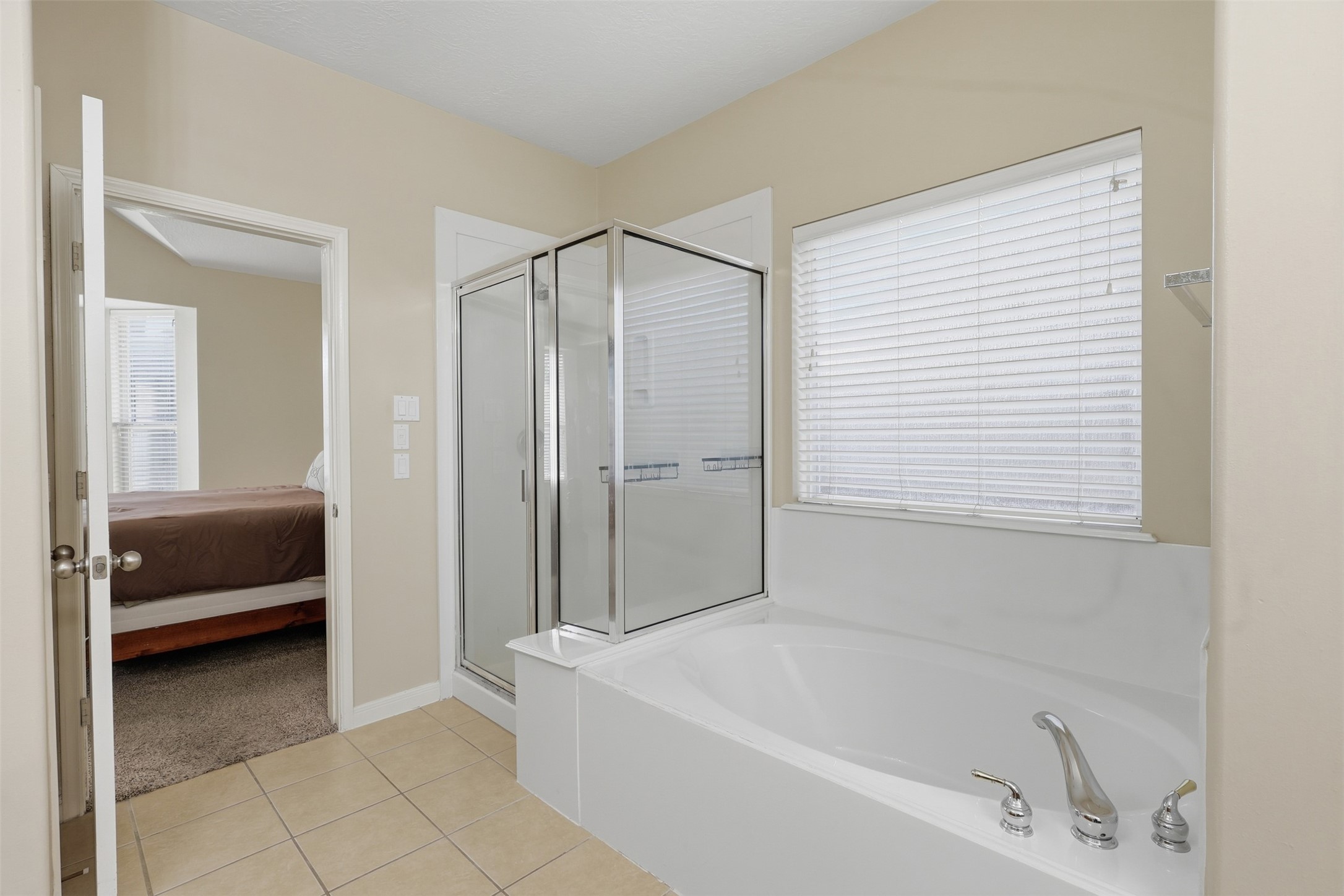 Beautifully appointed primary bath showcases the large soaking tub, separate glass-enclosed walk-in shower, dual vanity, and bright window. A spacious and inviting setting with plenty of room to start and unwind at the end of the day.