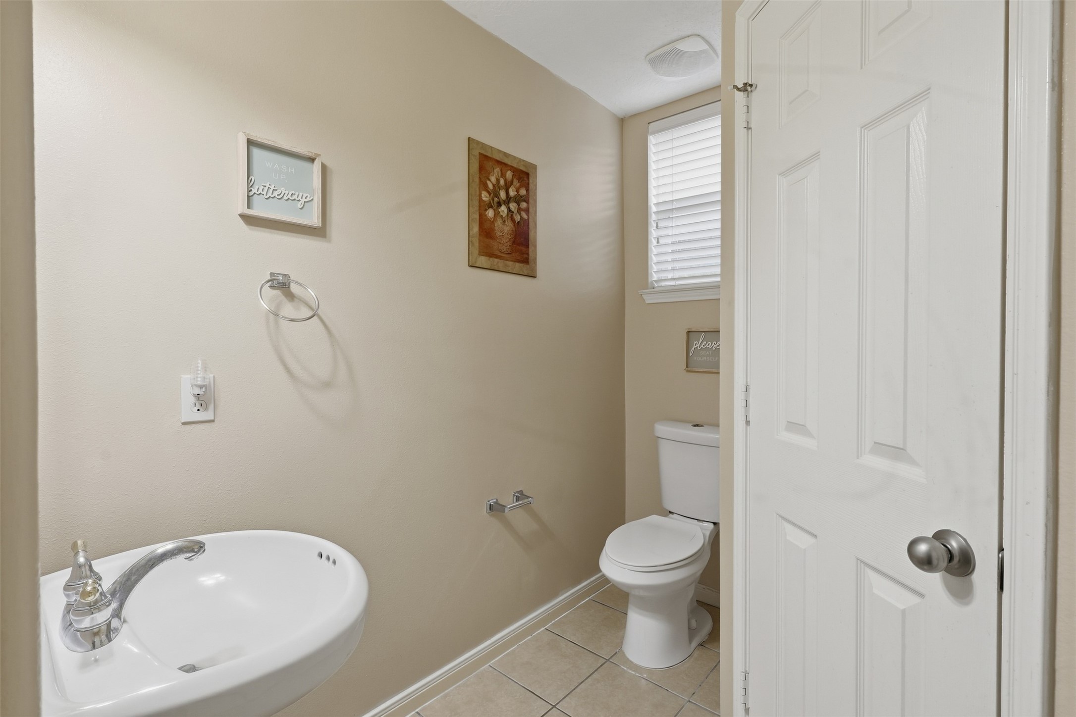 Convenient first-floor half bath features a clean, bright design with a pedestal sink, framed wall art, and tile flooringperfectly positioned for guests and everyday convenience.