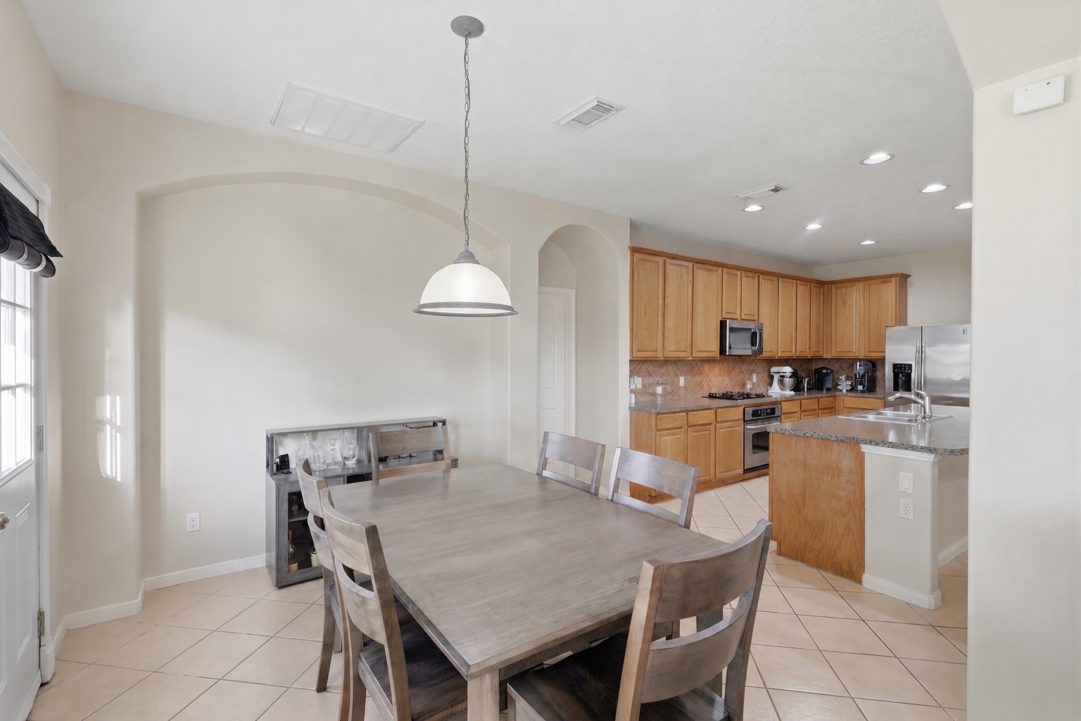 Bright breakfast area offers a comfortable setting for everyday dining, complemented by a stylish pendant light and abundant natural light. The open view into the spacious kitchen highlights the generous cabinetry, tile backsplash, and expansive island.