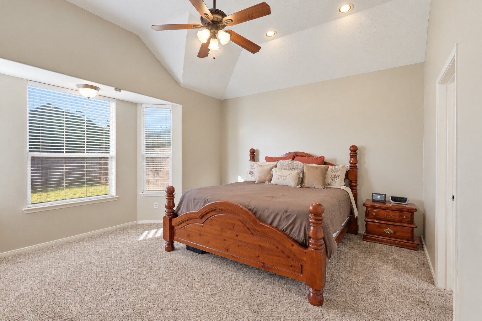 Spacious first-floor primary suite offers a peaceful retreat with plush carpeting, vaulted ceiling, ceiling fan, and large windows bringing in beautiful natural light in the sitting area. The generous layout provides plenty of space for a sitting area and comfortable furnishings.