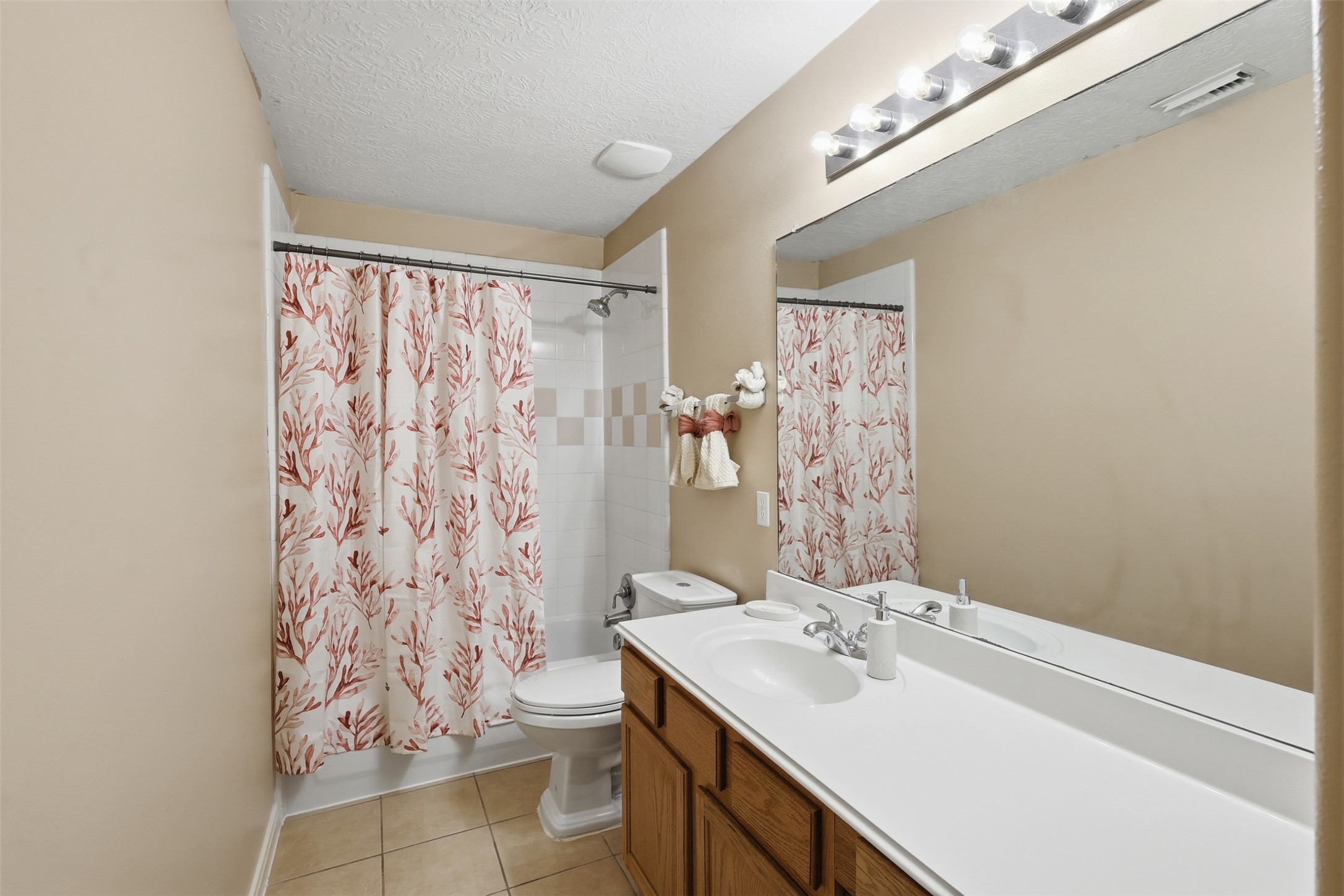 Bright secondary bathroom features a spacious vanity with ample counter space, large mirror, recessed lighting, and a tub/shower combination with decorative curtain. A clean and functional space designed for everyday convenience.