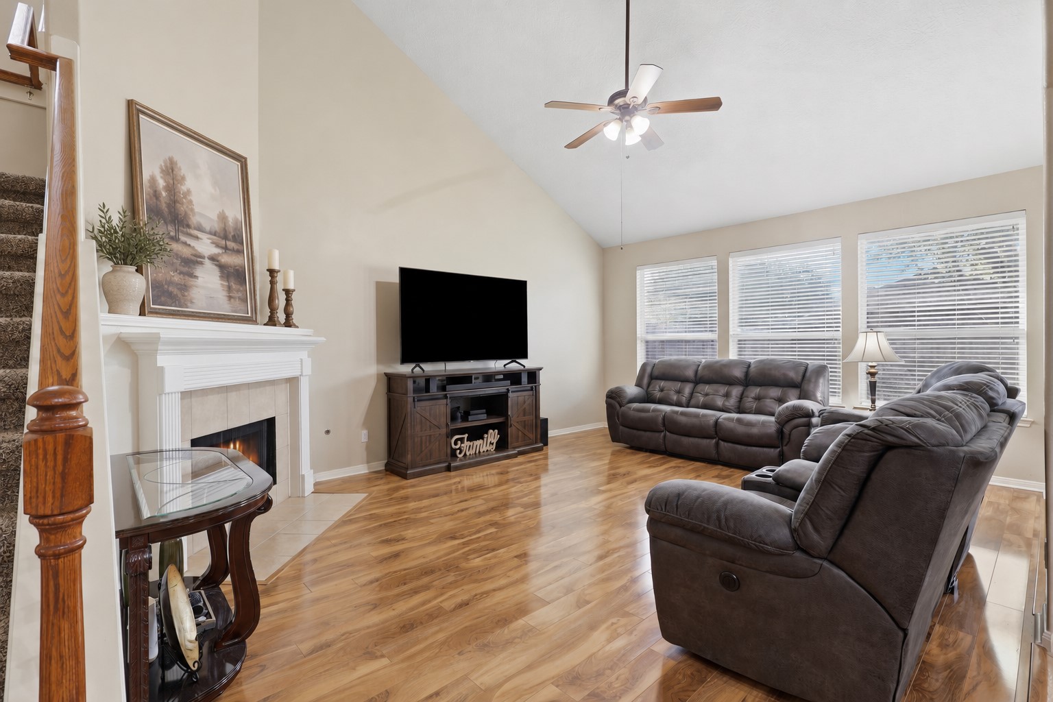 Warm and comfortable living space showcases the corner fireplace, soaring ceiling, ceiling fan, beautiful wood-look flooring, and large windows overlooking the backyard. Plenty of room for relaxing, movie nights, and gathering with family and friends.