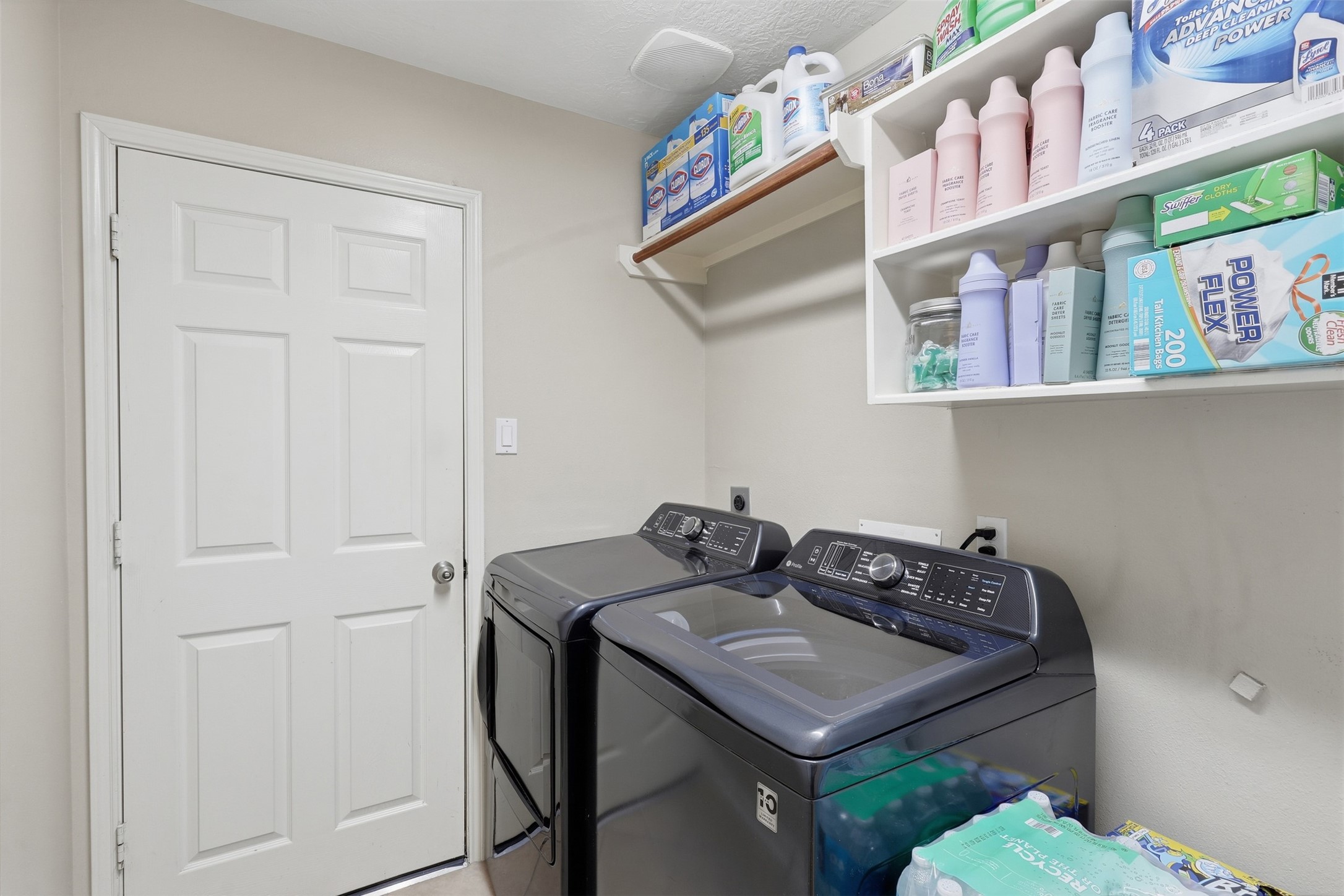 Convenient first-floor utility room features washer and dryer connections, overhead shelving for storage, and ample space for laundry essentials. A practical and organized workspace for everyday household needs.
