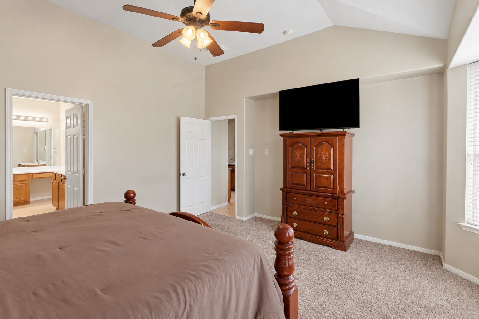 Another inviting view of the spacious primary suite showcases the vaulted ceiling, ceiling fan, large windows, and generous floor space. The bright, relaxing retreat offers plenty of room to unwind and connects conveniently to the luxurious primary bath.