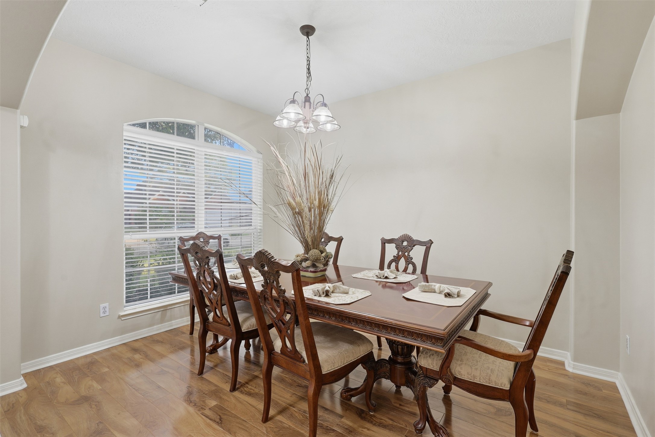 Gather in style in this bright and elegant formal dining room, where a large front window fills the space with natural light. Beautiful wood-look flooring, classic architectural arches, and a stunning chandelier create a warm and sophisticated atmosphere.